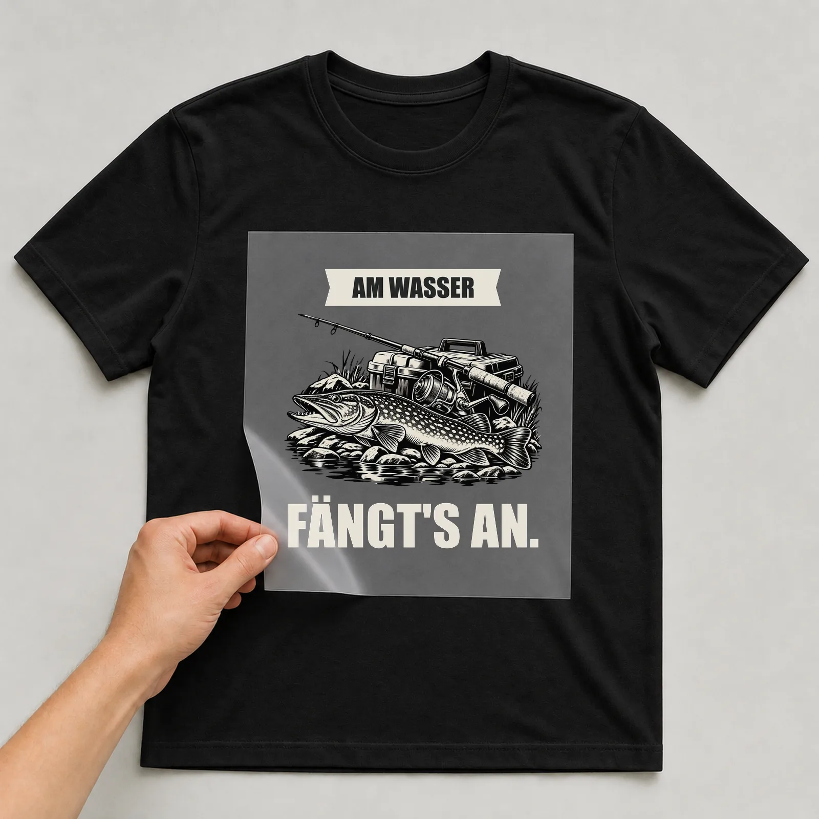 Bügelbild „Am Wasser fängt's an“ auf schwarzem T-Shirt, Folie wird aufgelegt