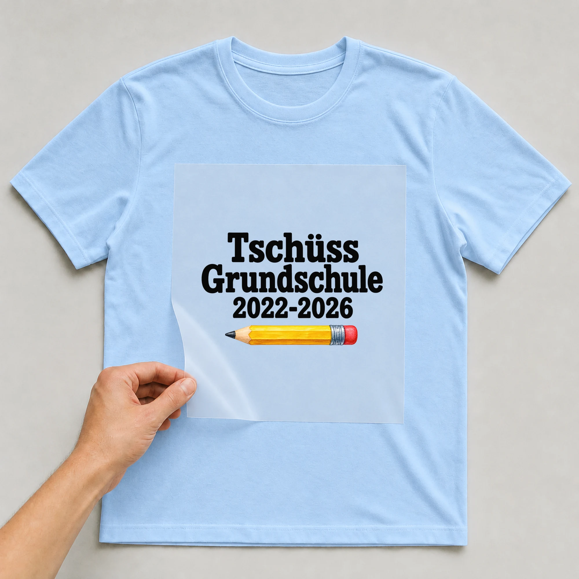 Bügelbild „Tschüss Grundschule 2022-2026“ auf babyblauem T-Shirt, Folie wird aufgelegt