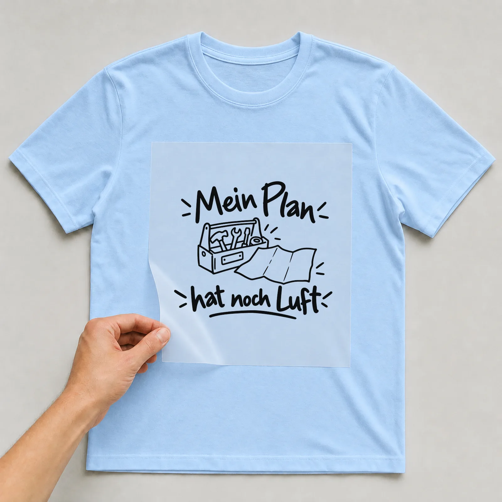 Bügelbild „Mein Plan hat noch Luft“ auf hellblauem T-Shirt, Folie wird aufgelegt