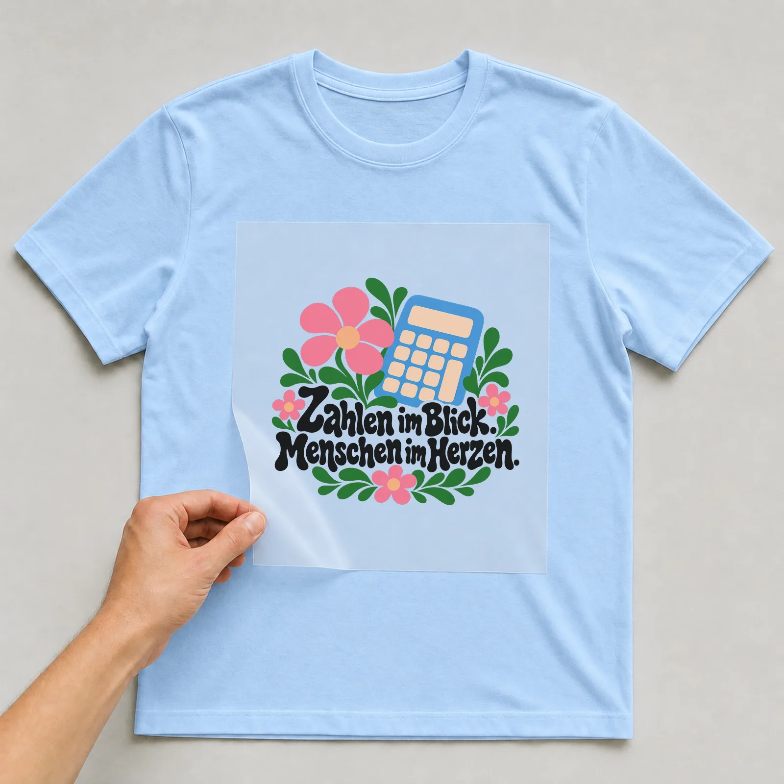 Bügelbild „Zahlen im Blick. Menschen im Herzen.“ auf hellblauem T-Shirt, Folie wird aufgelegt