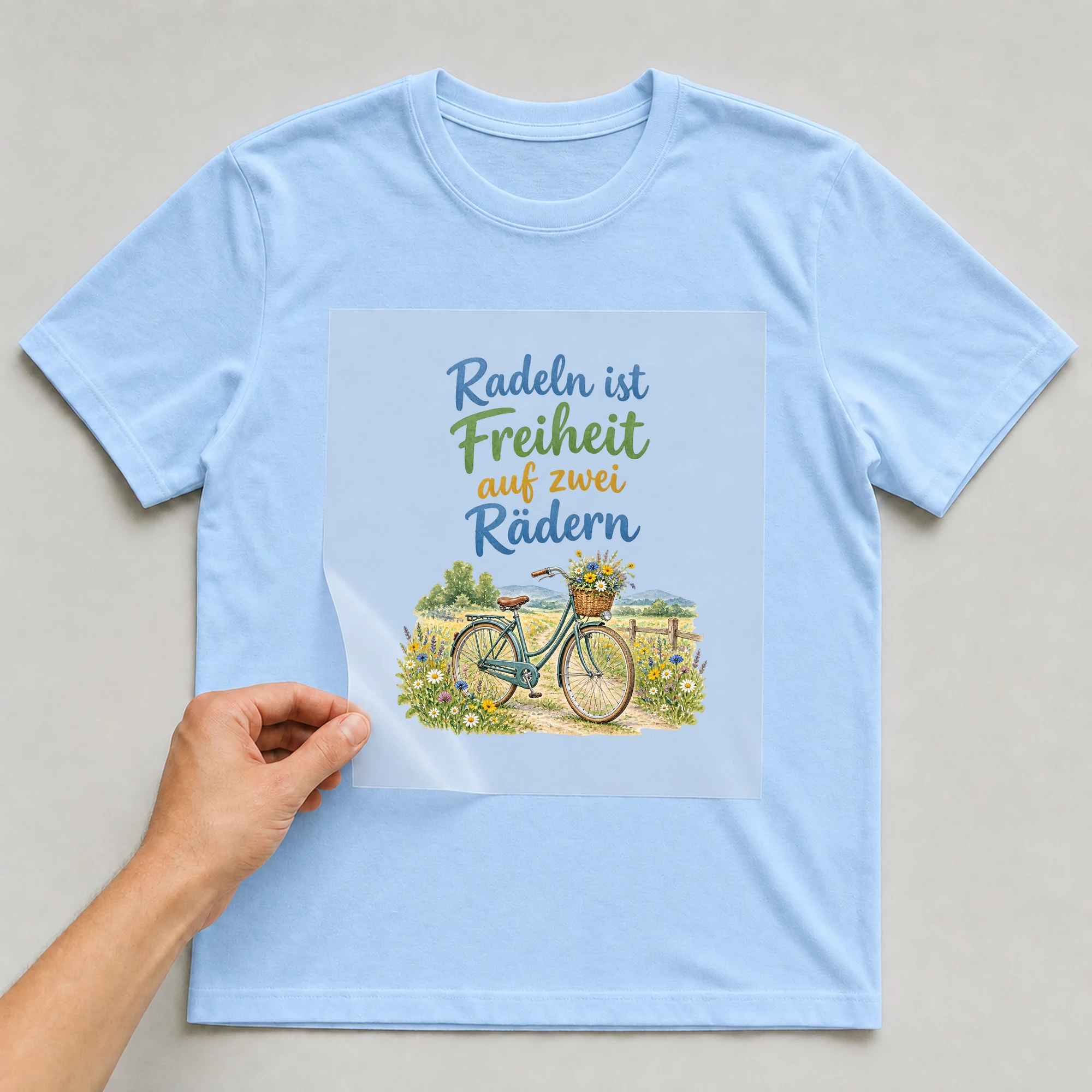 Bügelbild „Radeln ist Freiheit auf zwei Rädern“ auf babyblauem T-Shirt, Folie wird aufgelegt