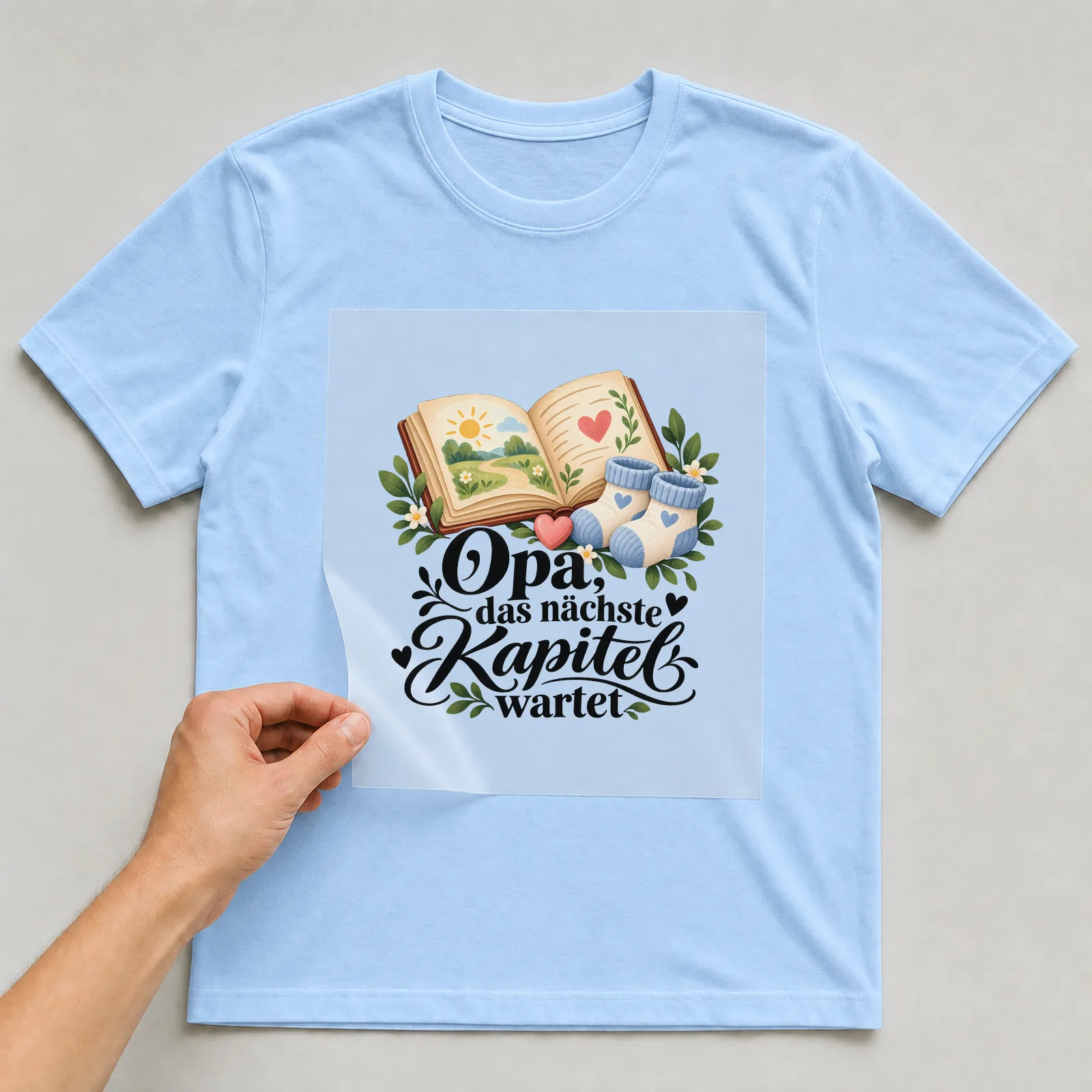 Bügelbild „Opa, das nächste Kapitel wartet“ auf hellblauem T-Shirt, Folie wird aufgelegt