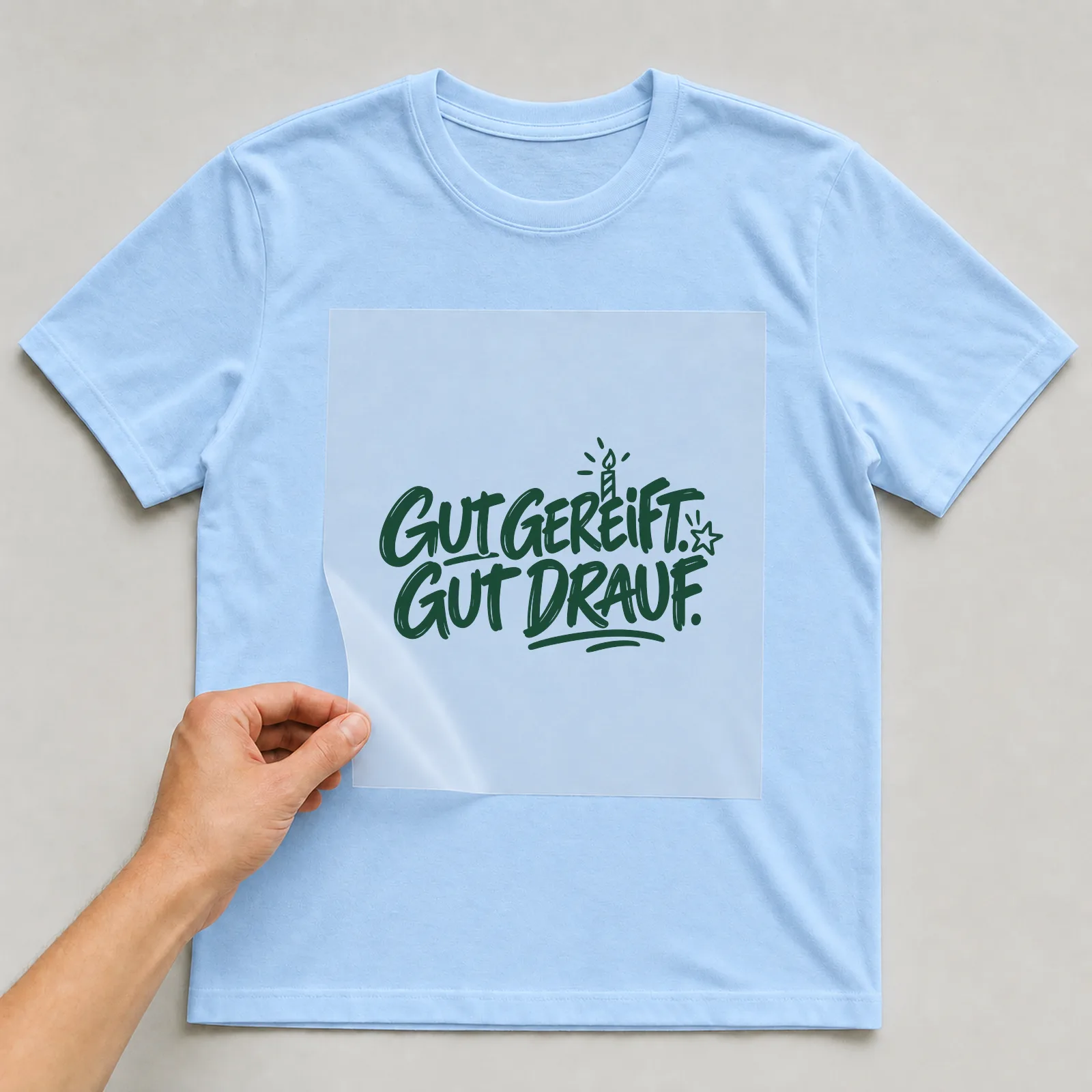 Bügelbild „Gut gereift. Gut drauf.“ auf hellblauem T-Shirt, Folie wird aufgelegt