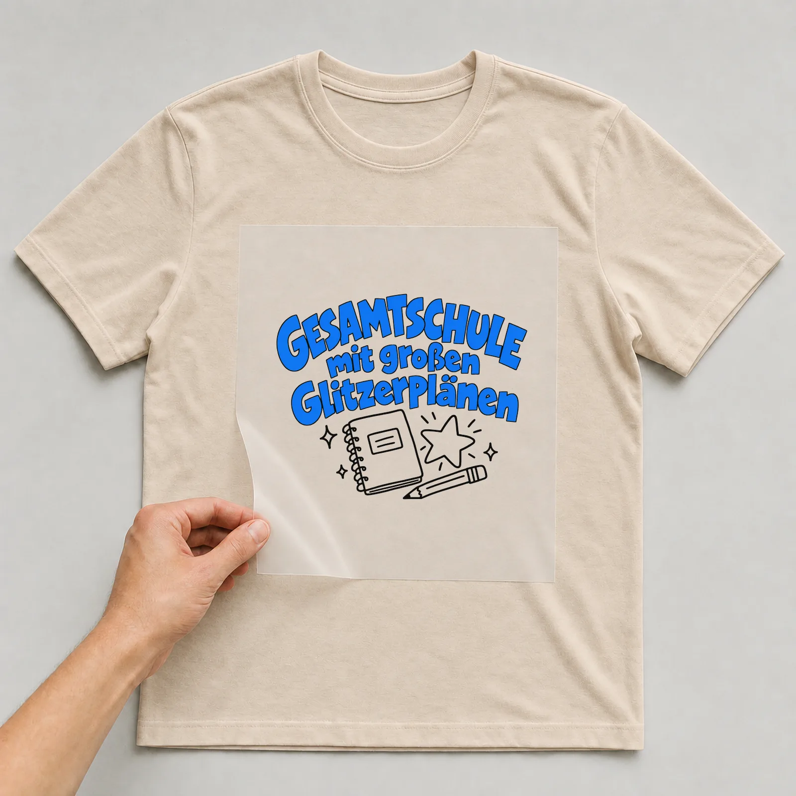 Bügelbild „Gesamtschule mit großen Glitzerplänen“ auf beigem T-Shirt, Folie wird aufgelegt