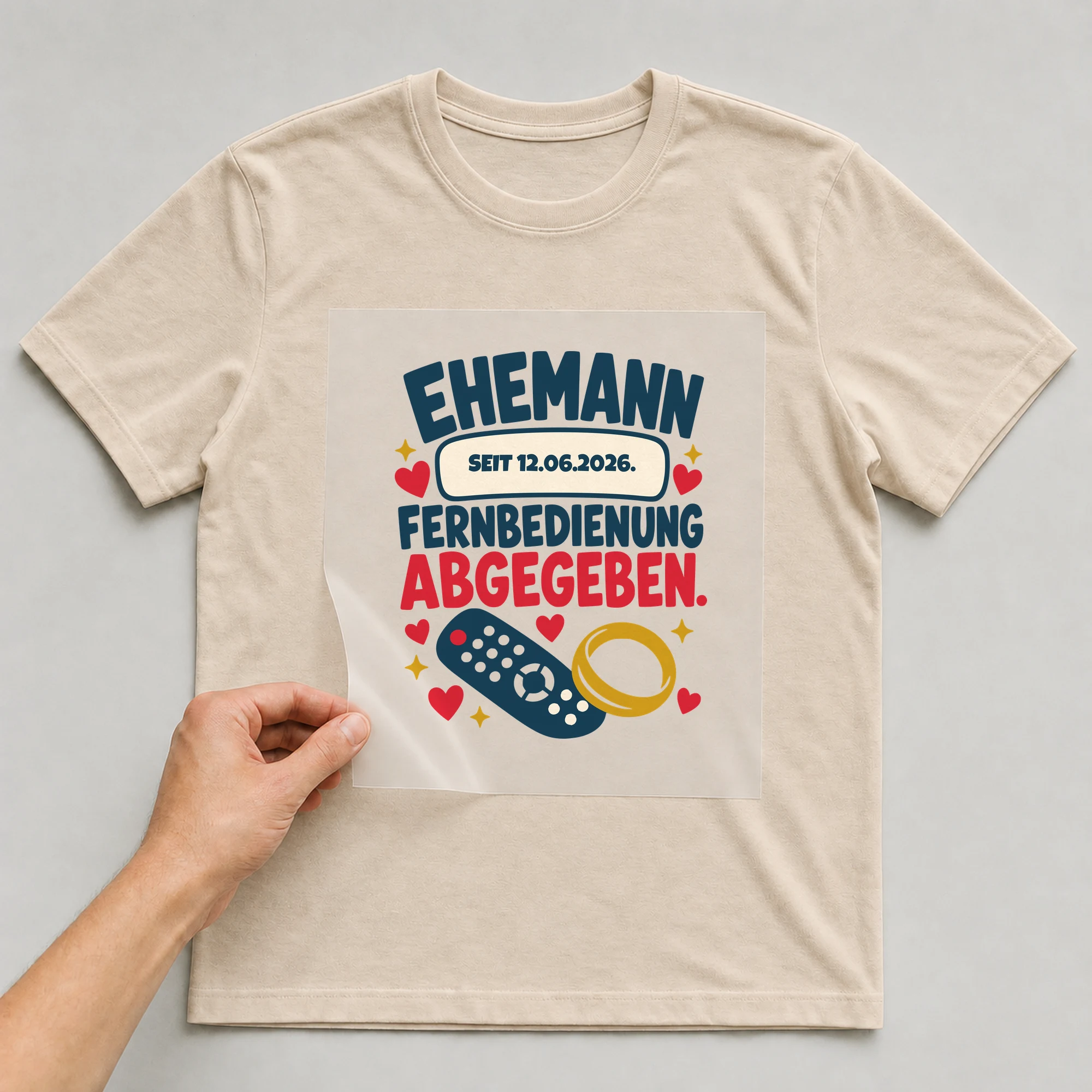 Bügelbild Ehemann. Fernbedienung abgegeben. mit Datum auf beigem T-Shirt, Folie wird aufgelegt