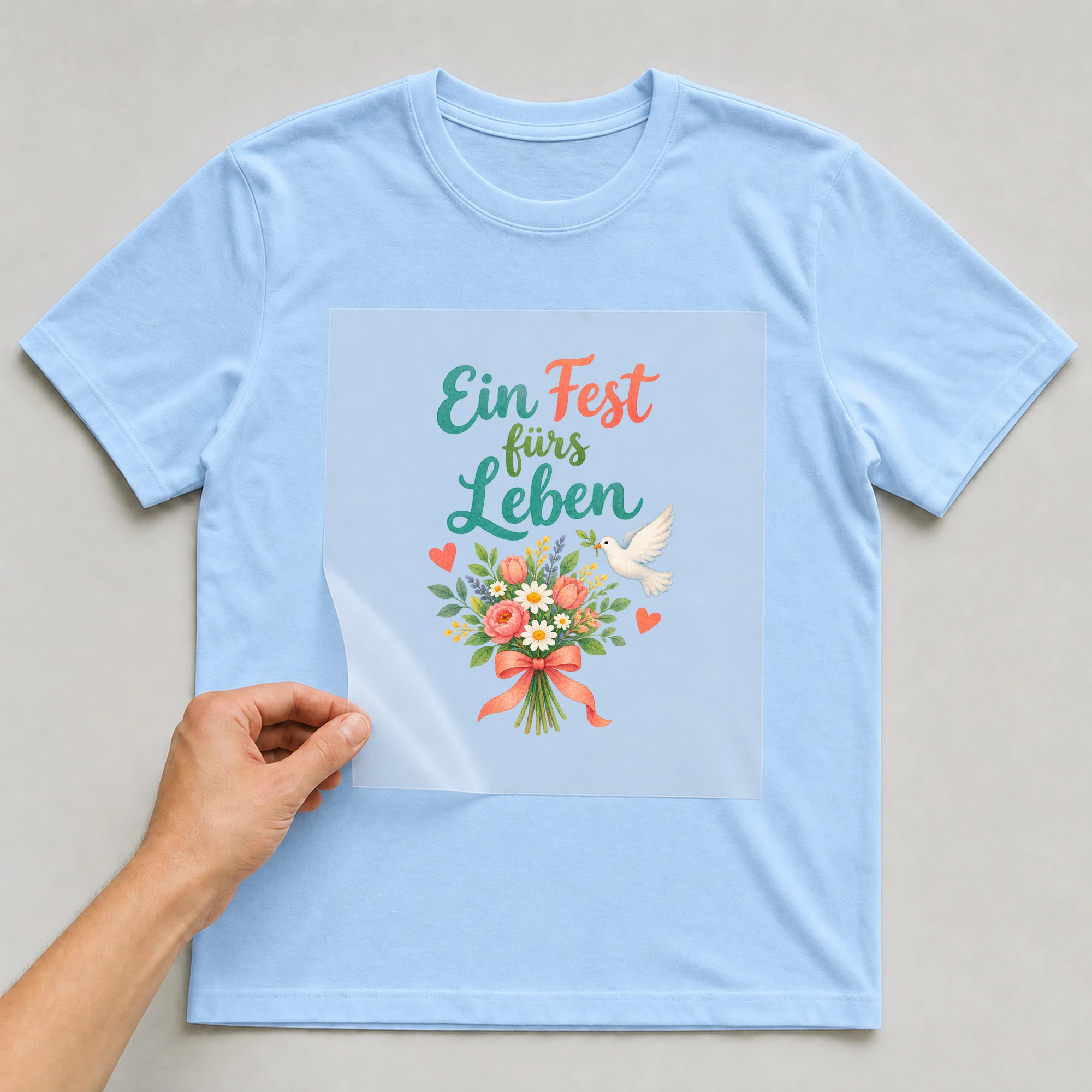 Bügelbild „Ein Fest fürs Leben“ auf babyblauem T-Shirt, Folie wird aufgelegt