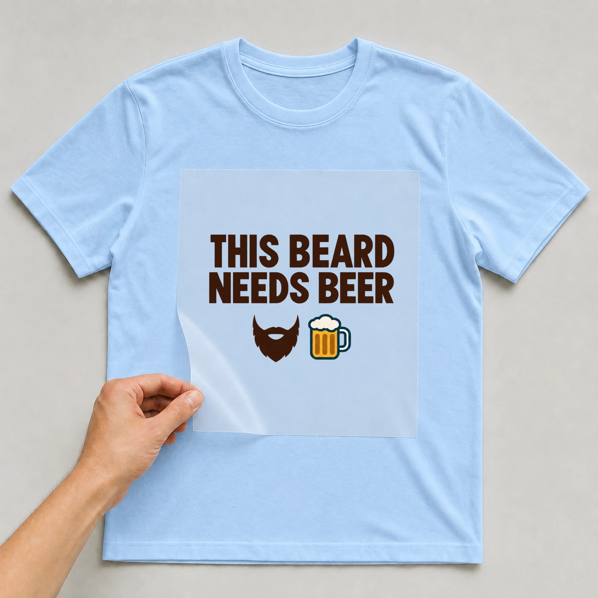 Bügelbild „THIS BEARD NEEDS BEER“ auf babyblauem T-Shirt, Folie wird aufgelegt