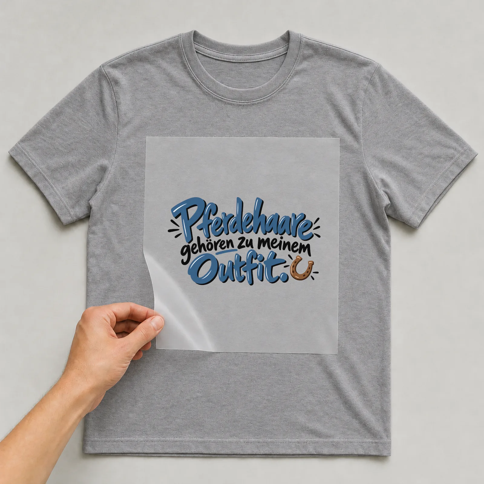 Bügelbild „Pferdehaare gehören zu meinem Outfit“ auf grauem T-Shirt, Folie wird aufgelegt