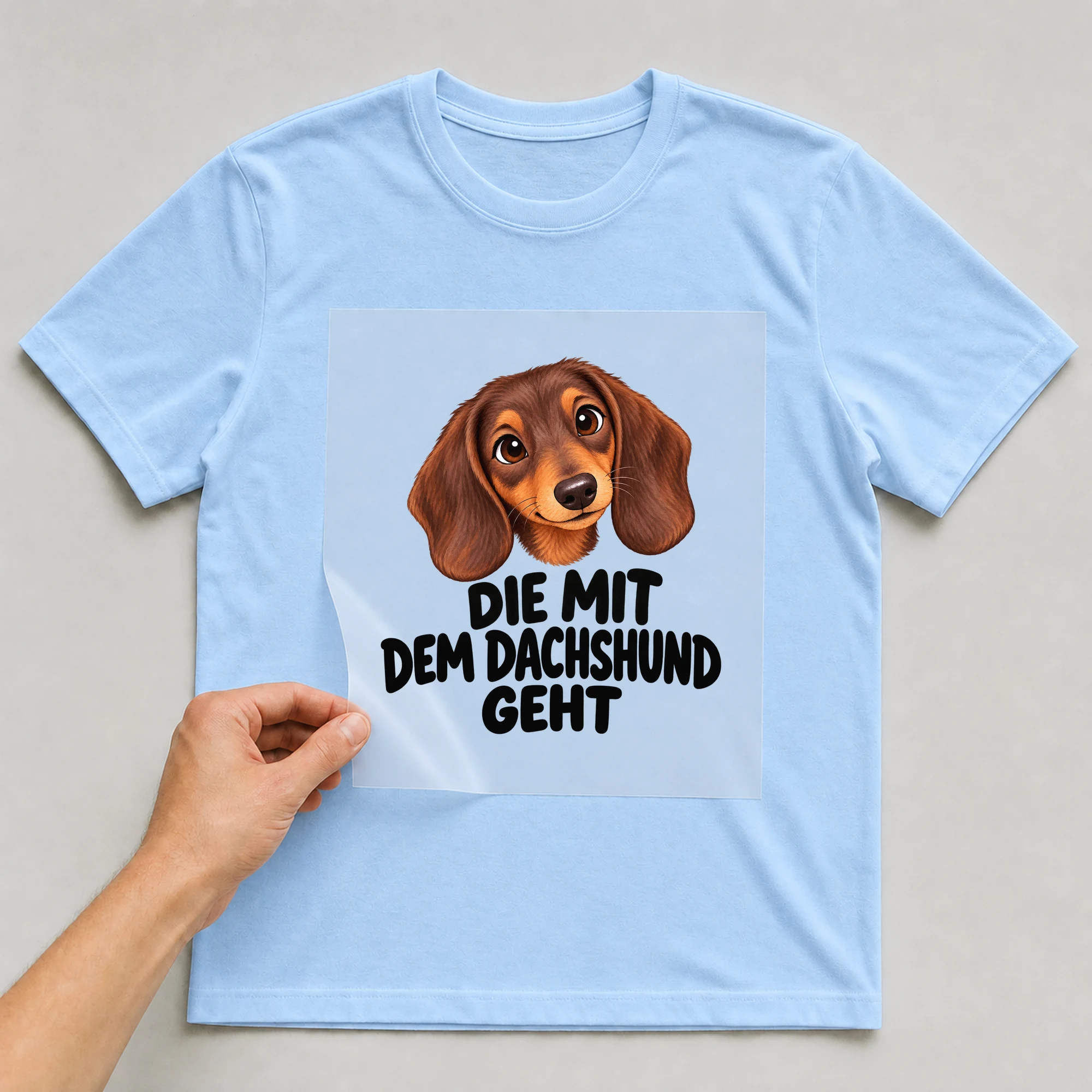 Bügelbild „Die mit dem Dachshund geht“ auf babyblauem T-Shirt, Folie wird aufgelegt