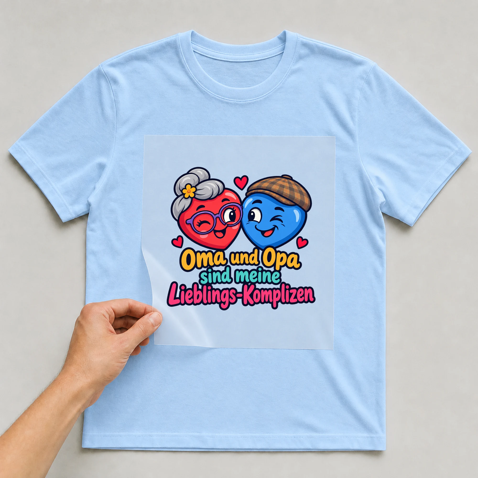Bügelbild „Oma und Opa sind meine Lieblings-Komplizen“ auf babyblauem T-Shirt, Folie wird aufgelegt