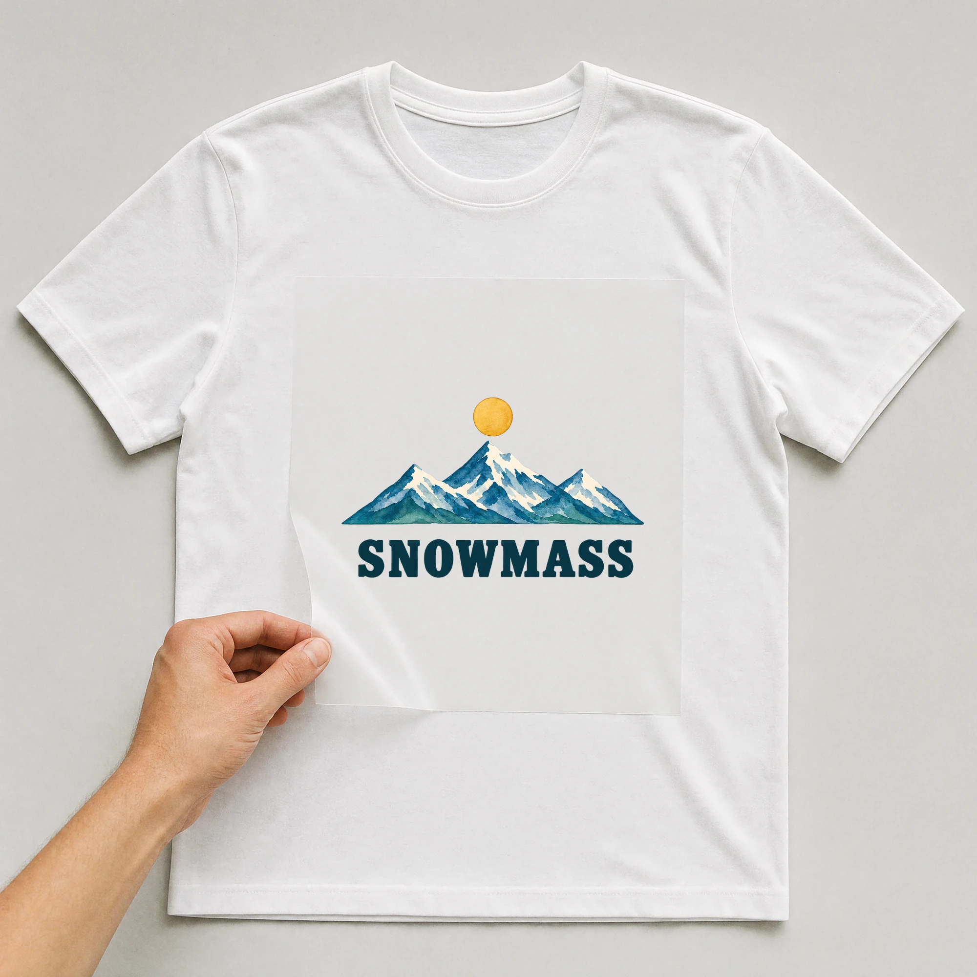 Bügelbild „SNOWMASS“ auf weißem T-Shirt, Folie wird aufgelegt