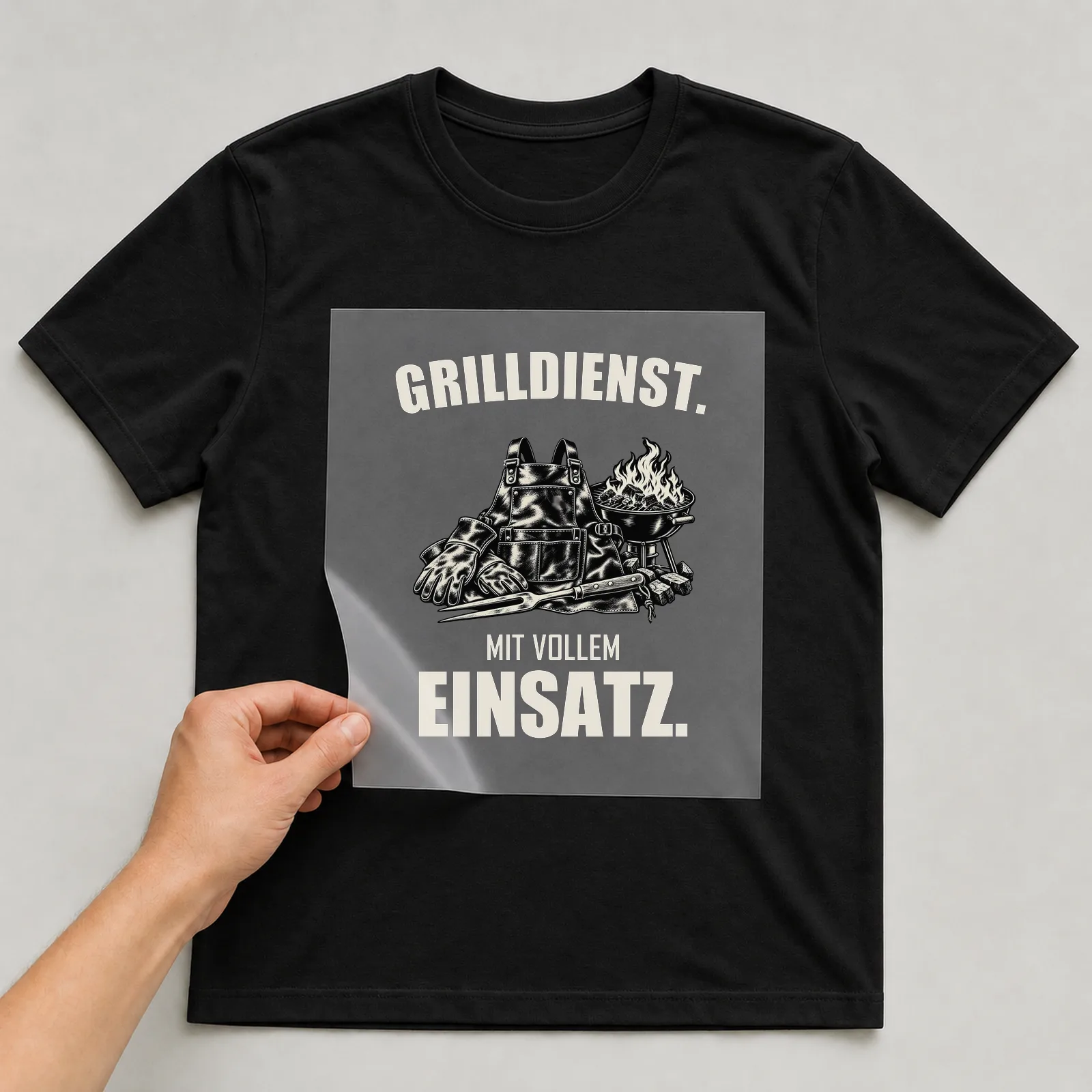 Bügelbild „Grilldienst. Mit vollem Einsatz.“ auf schwarzem T-Shirt, Folie wird aufgelegt
