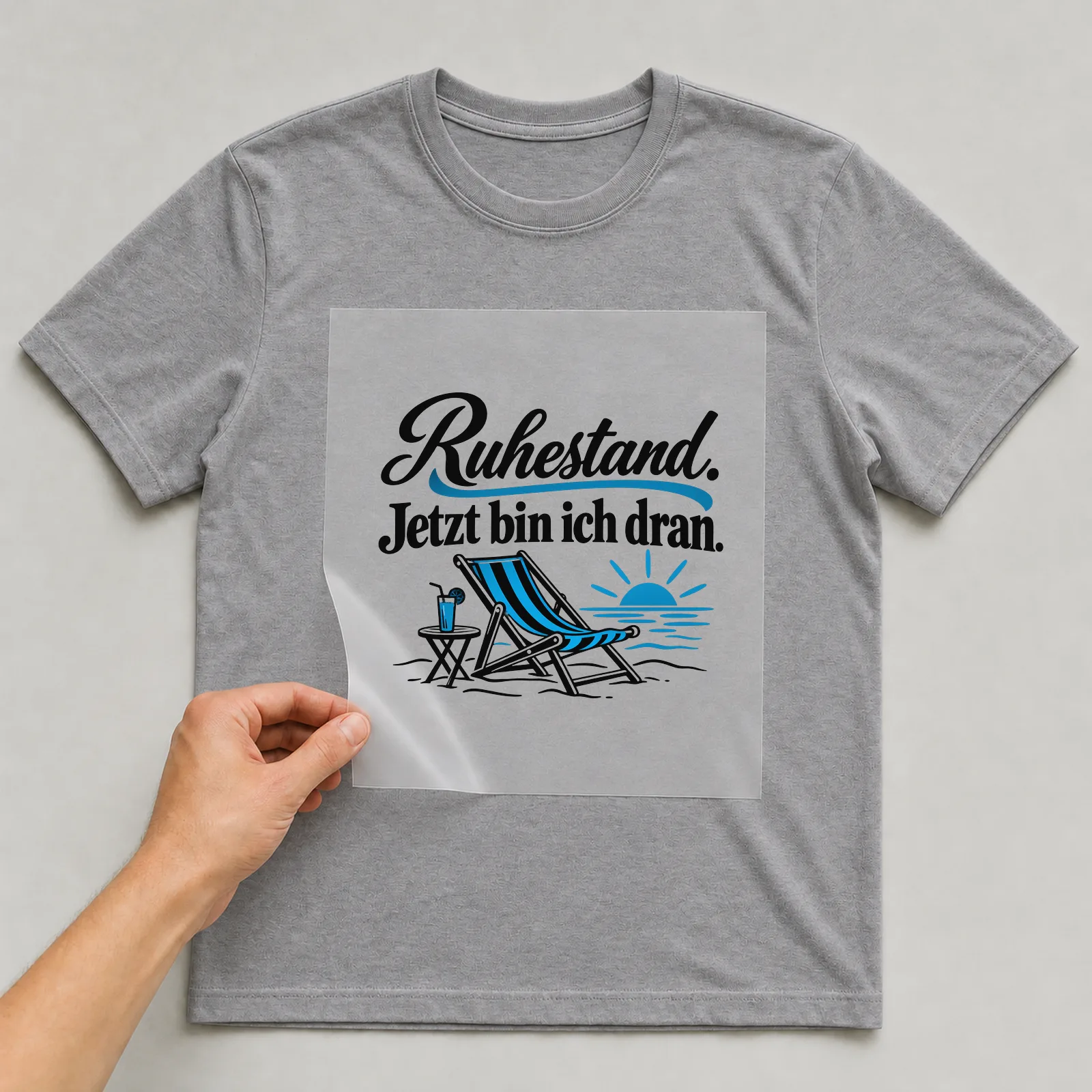 Bügelbild „Ruhestand. Jetzt bin ich dran.“ auf grauem T-Shirt, Folie wird aufgelegt
