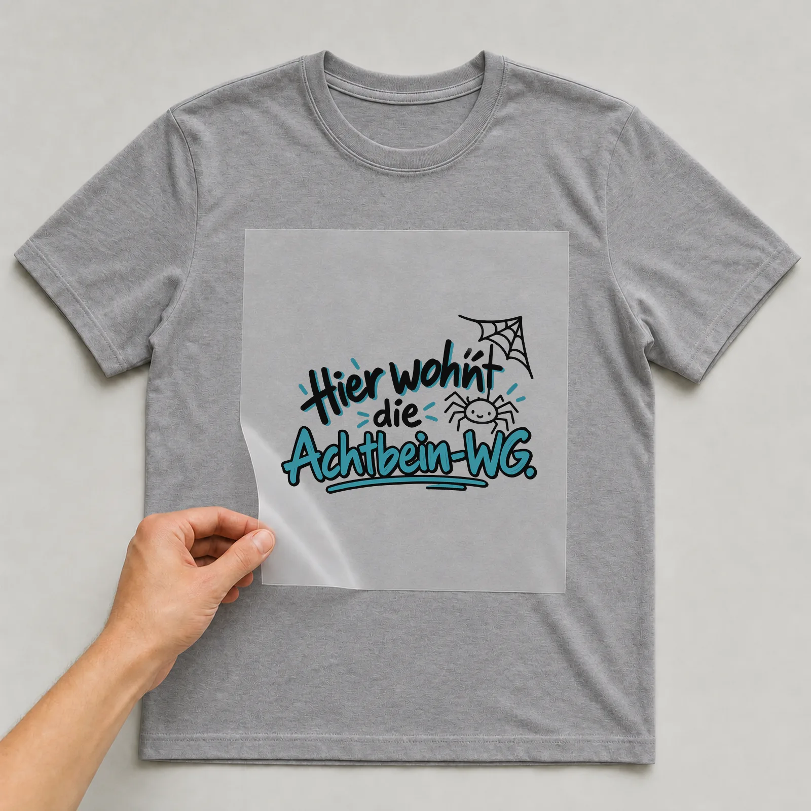 Bügelbild „Hier wohnt die Achtbein-WG“ auf grauem T-Shirt, Folie wird aufgelegt