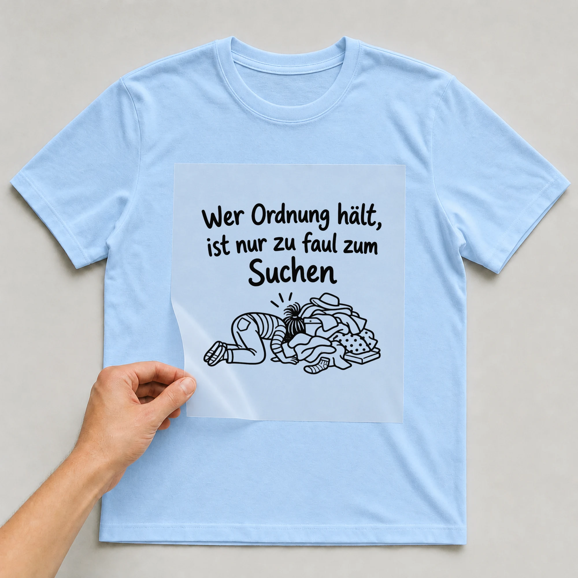 Bügelbild „Wer Ordnung hält, ist nur zu faul zum Suchen“ auf babyblauem T-Shirt, Folie wird aufgelegt