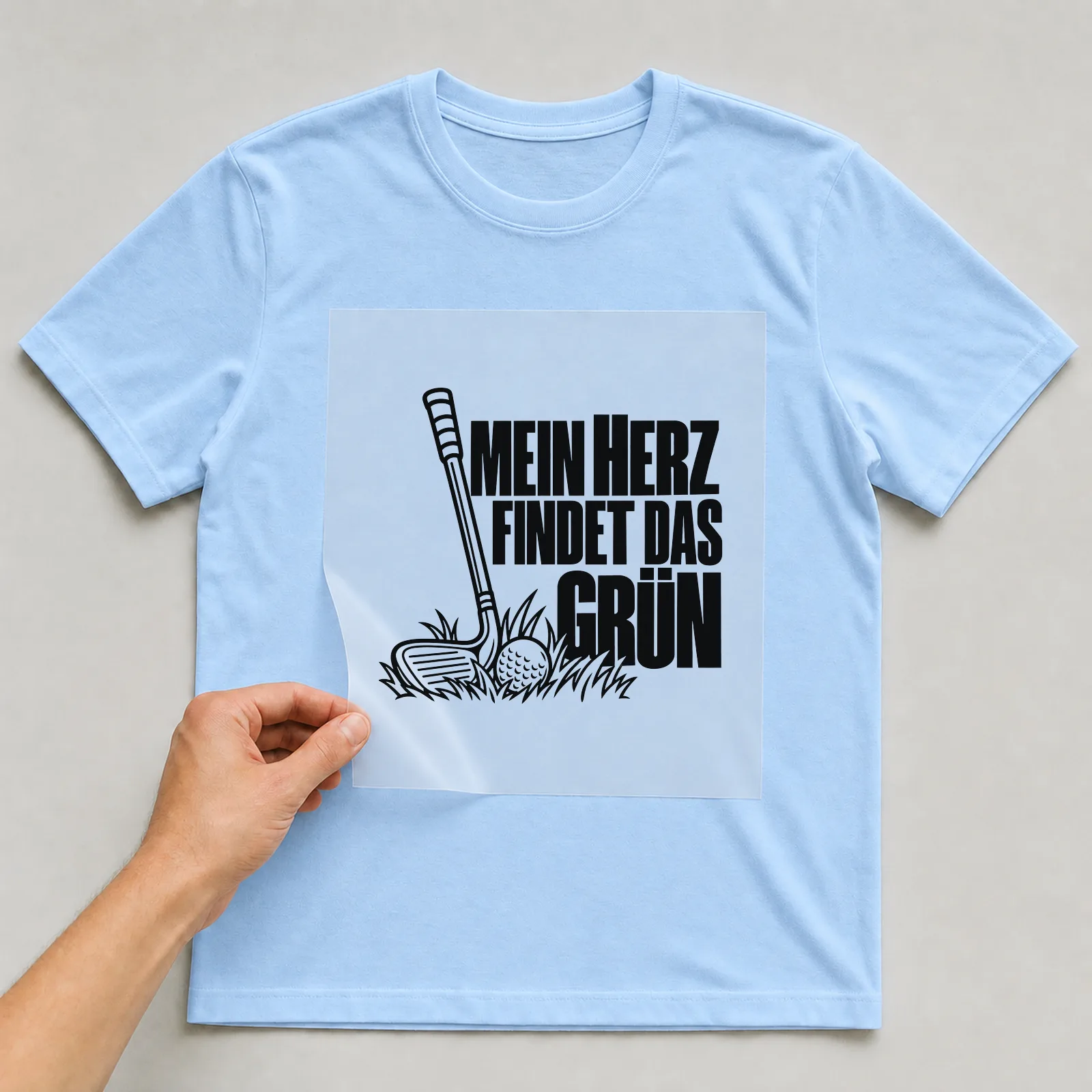 Bügelbild „Mein Herz findet das Grün“ auf hellblauem T-Shirt, Folie wird aufgelegt