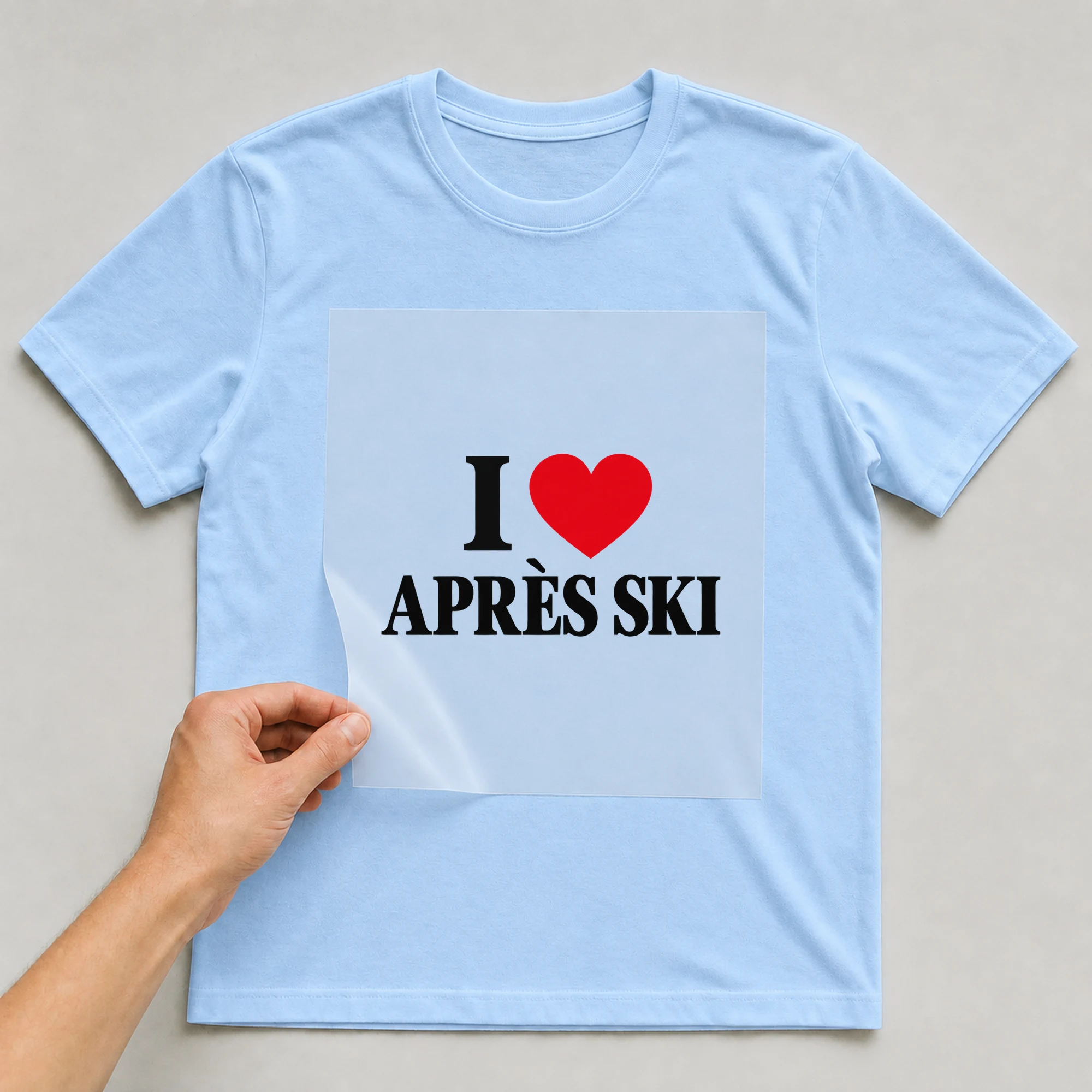Bügelbild „I Après Ski“ auf babyblauem T-Shirt, Folie wird aufgelegt