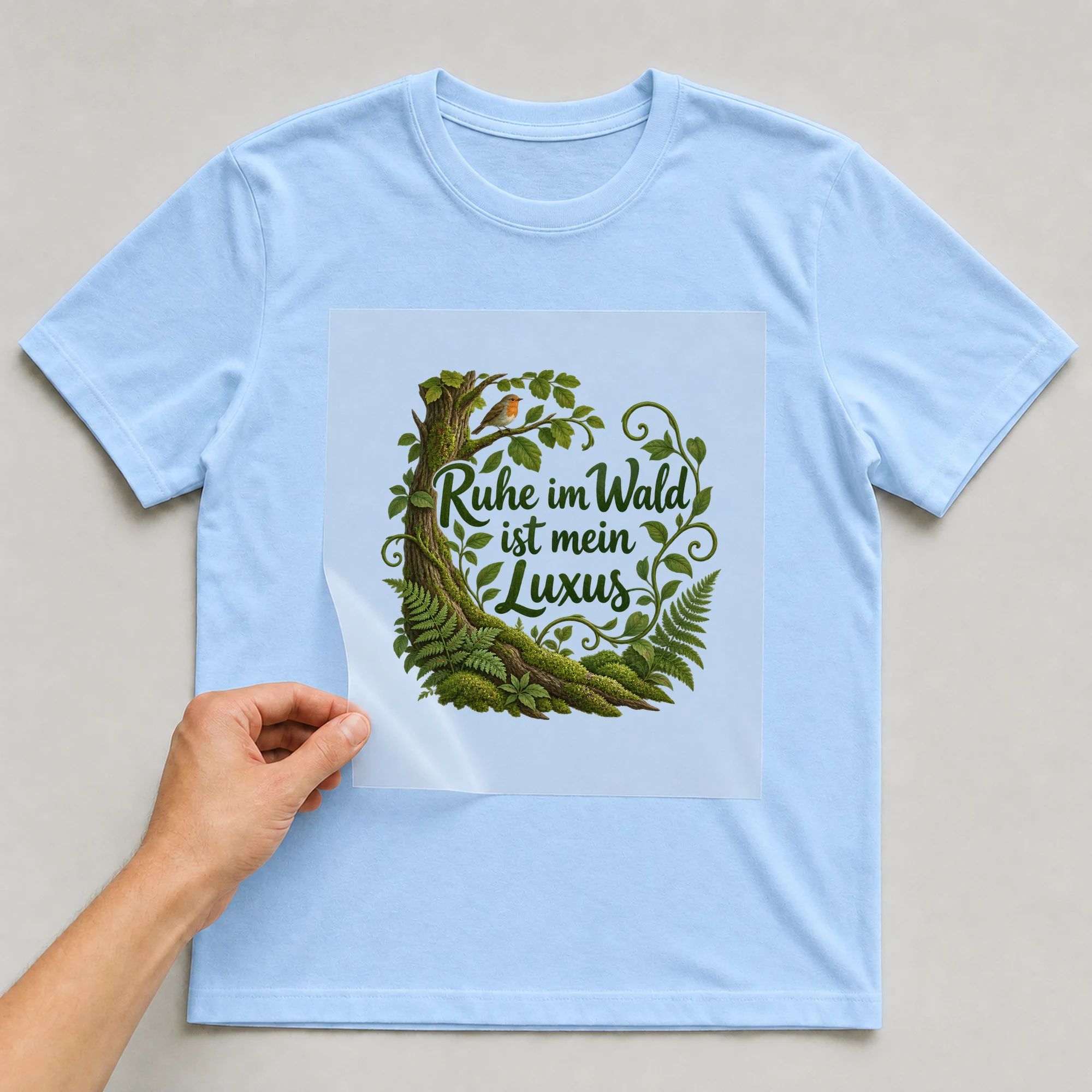 Bügelbild „Ruhe im Wald ist mein Luxus“ auf babyblauem T-Shirt, Folie wird aufgelegt