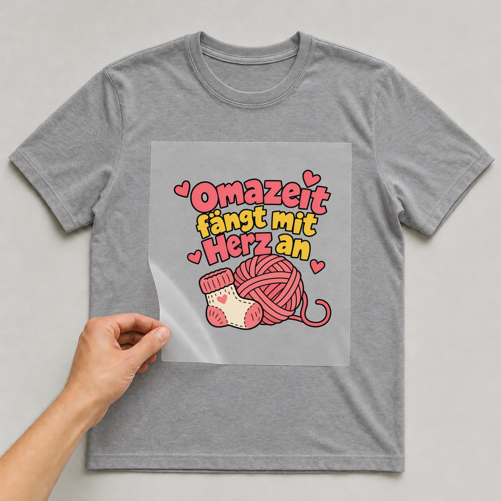 Bügelbild „Omazeit fängt mit Herz an“ auf grauem T-Shirt, Folie wird aufgelegt