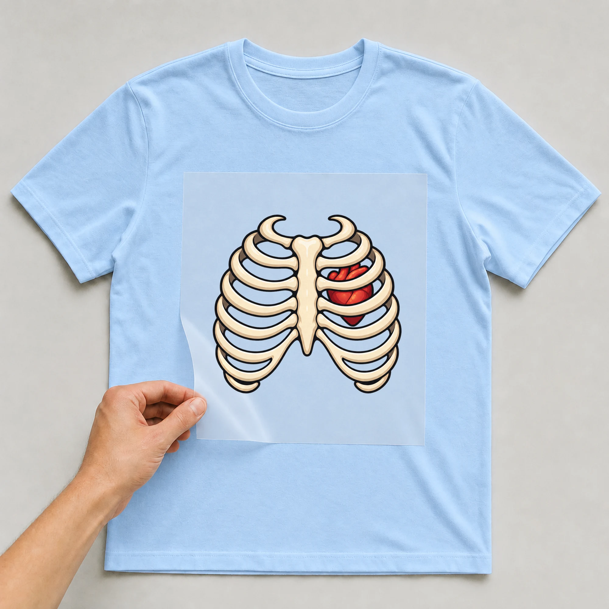 Bügelbild „Skelett Mit Herz“ auf babyblauem T-Shirt, Folie wird aufgelegt