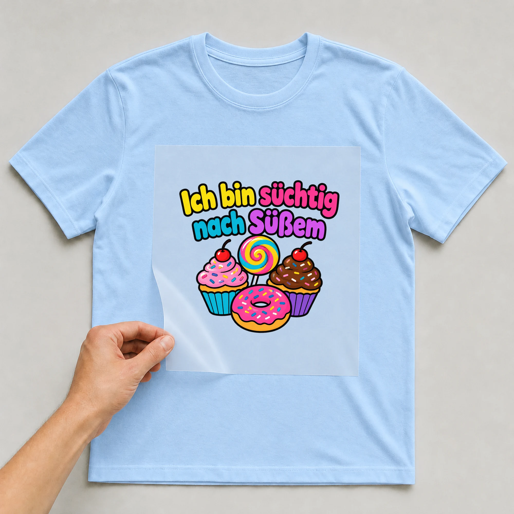 Bügelbild „Ich bin süchtig nach Süßem“ auf babyblauem T-Shirt, Folie wird aufgelegt