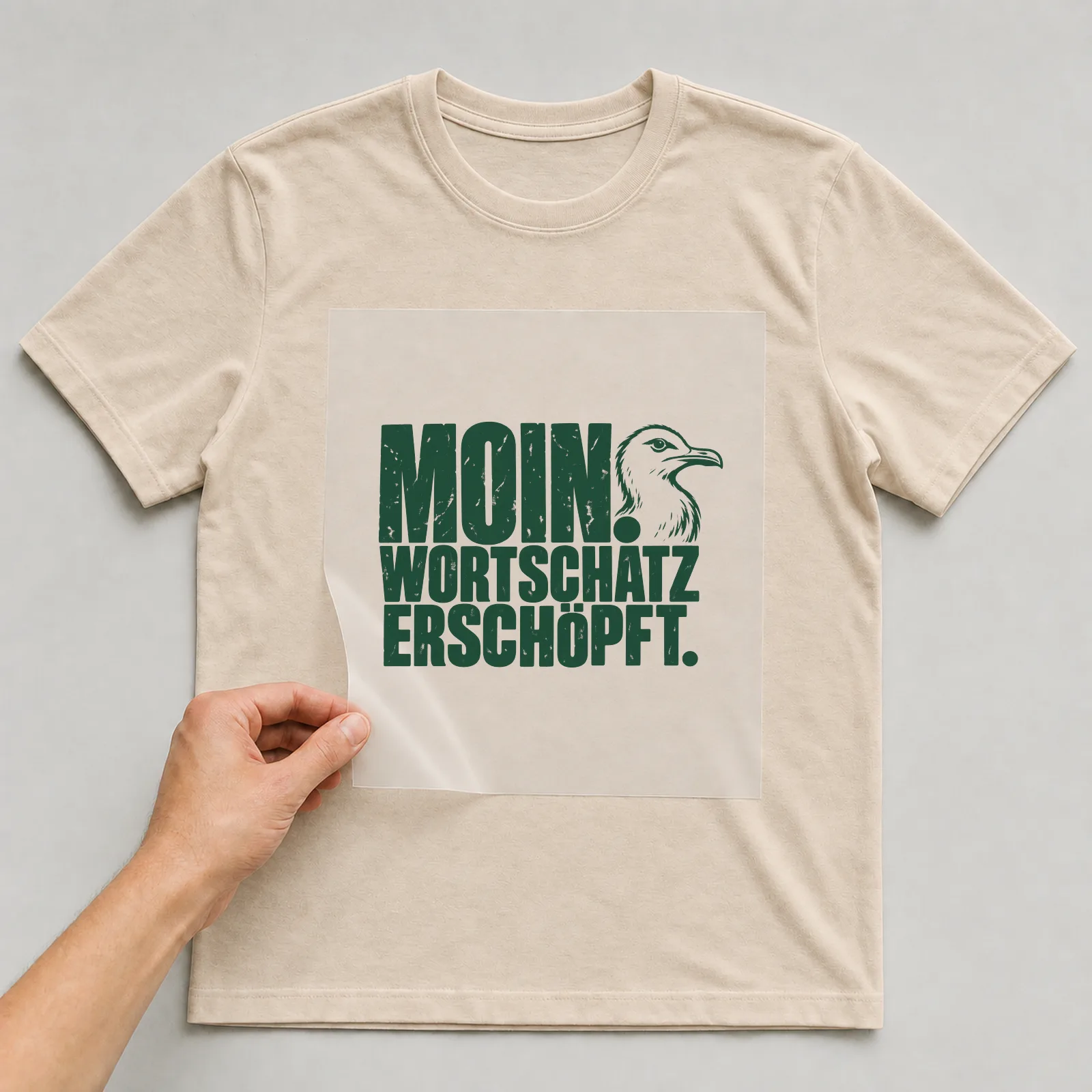Bügelbild „Moin. Wortschatz erschöpft.“ auf beigem T-Shirt, Folie wird aufgelegt