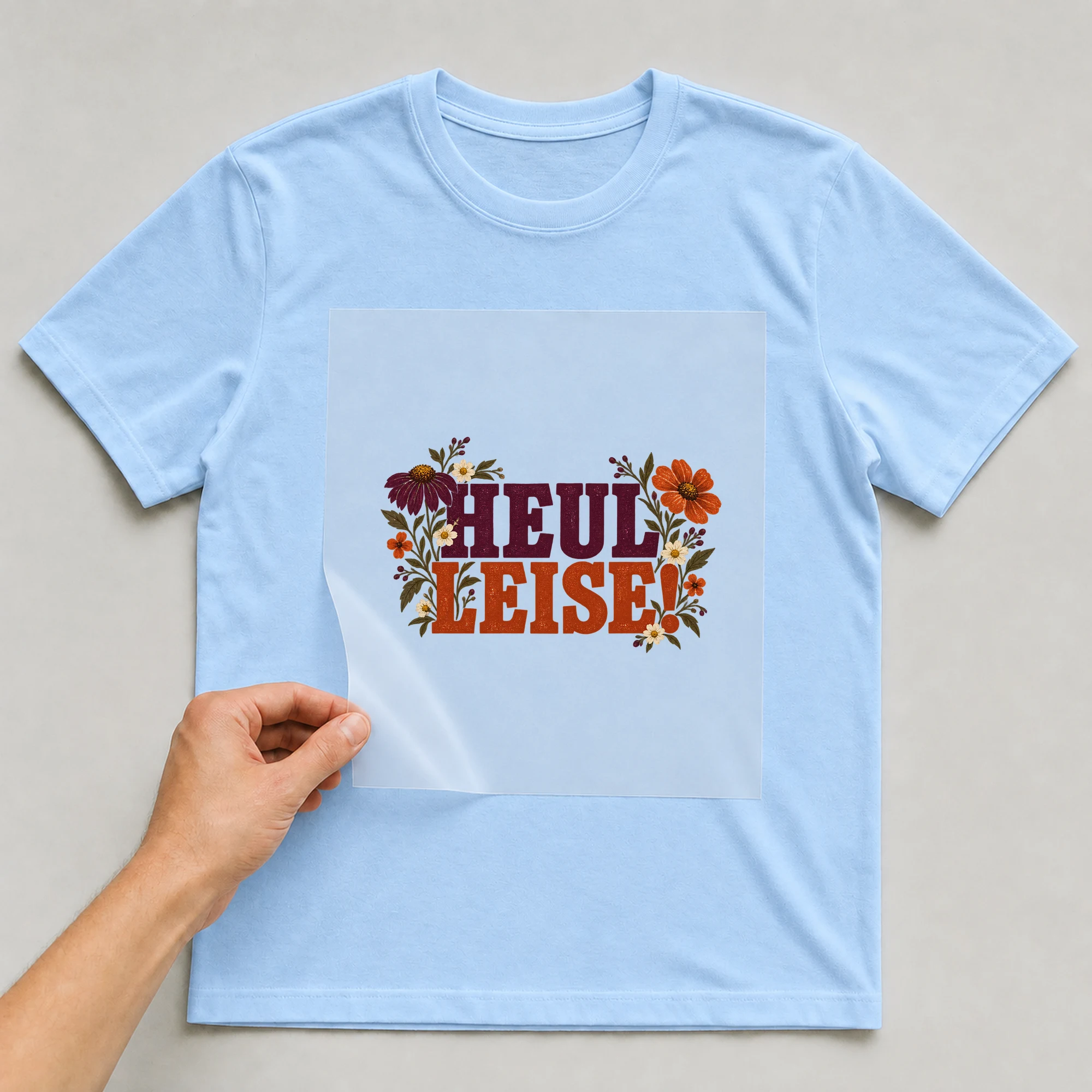 Bügelbild „Heul Leise!“ auf babyblauem T-Shirt, Folie wird aufgelegt