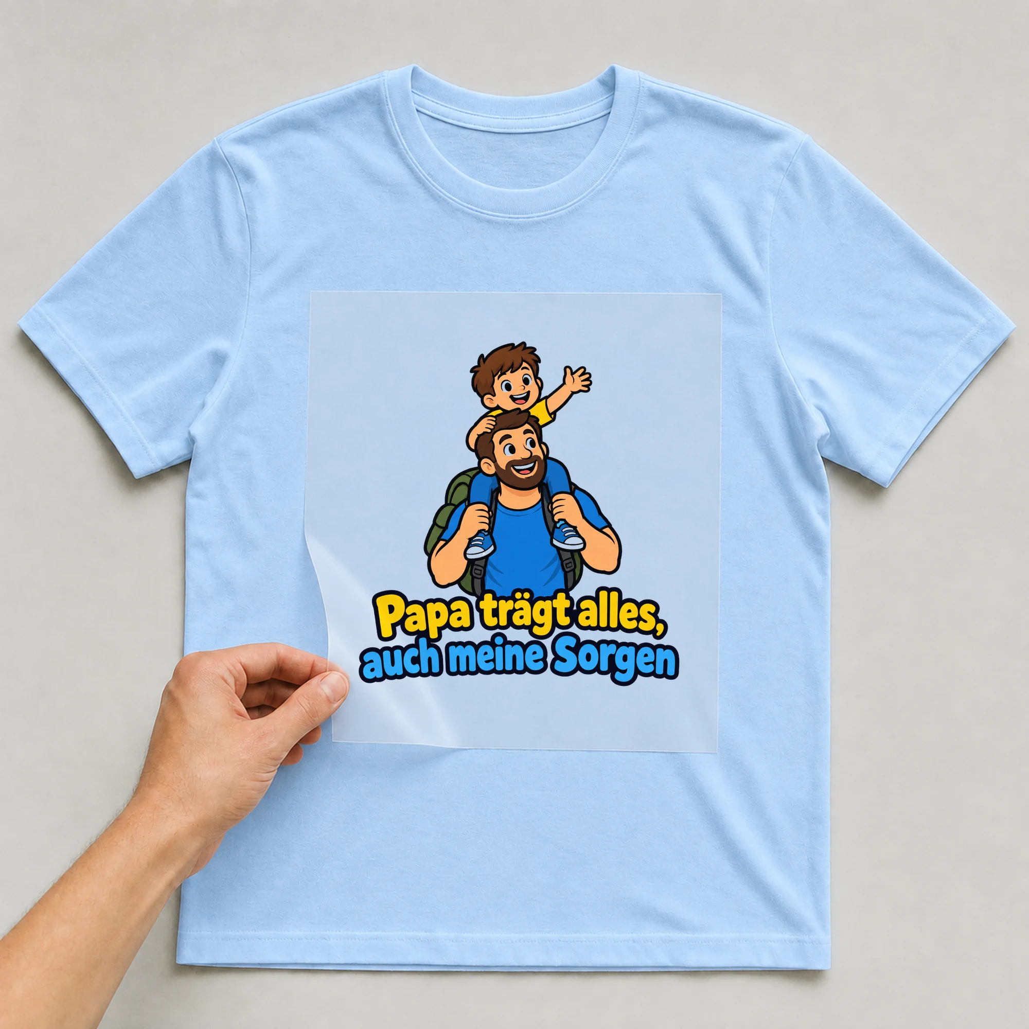 Bügelbild „Papa trägt alles, auch meine Sorgen“ auf babyblauem T-Shirt, Folie wird aufgelegt