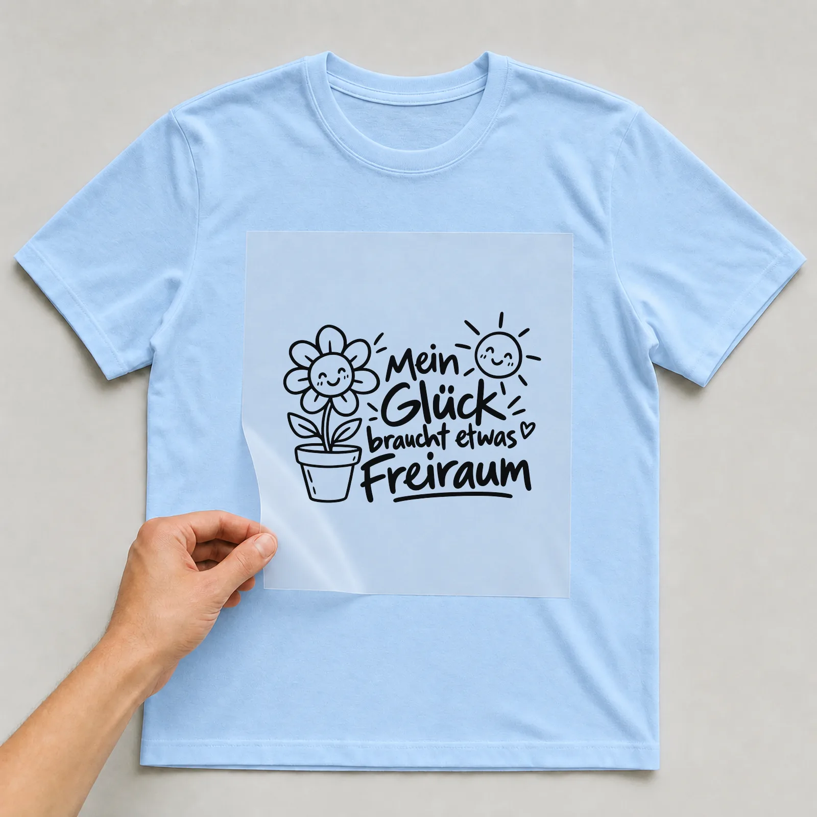 Bügelbild „Mein Glück braucht etwas Freiraum“ auf hellblauem T-Shirt, Folie wird aufgelegt