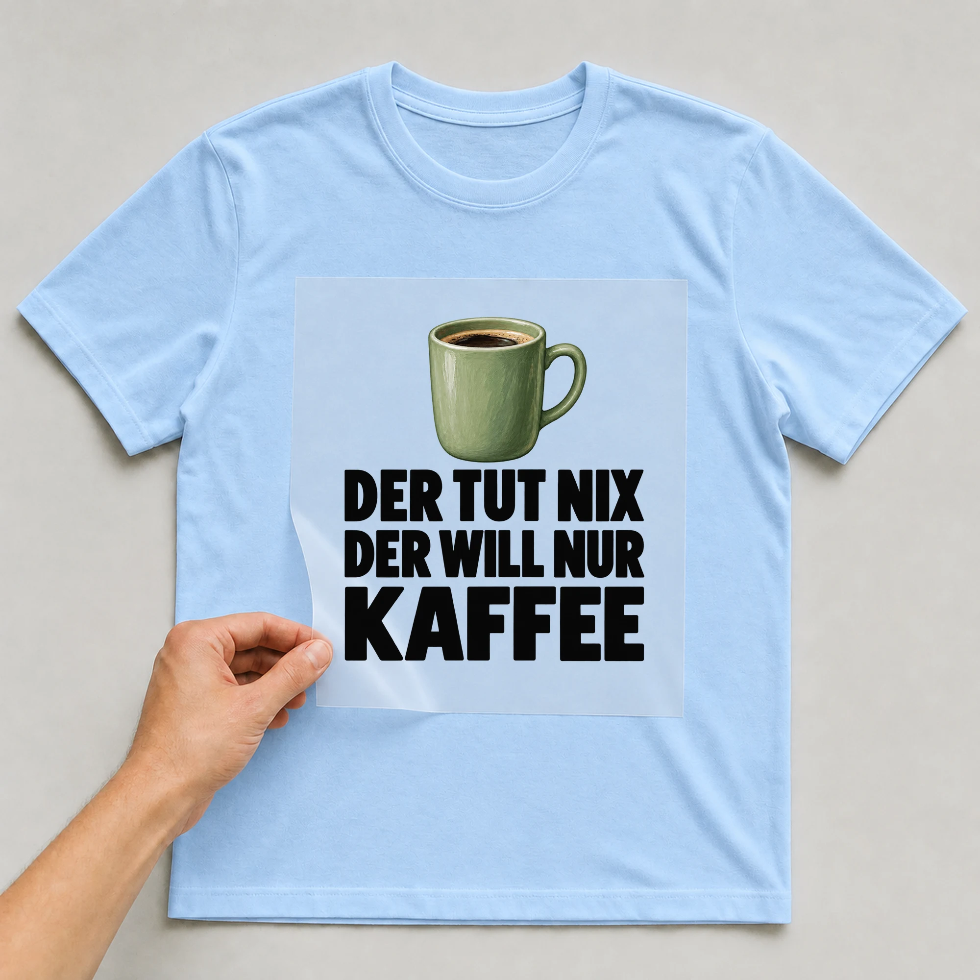 Bügelbild „Der tut nix der will nur Kaffee“ auf babyblauem T-Shirt, Folie wird aufgelegt