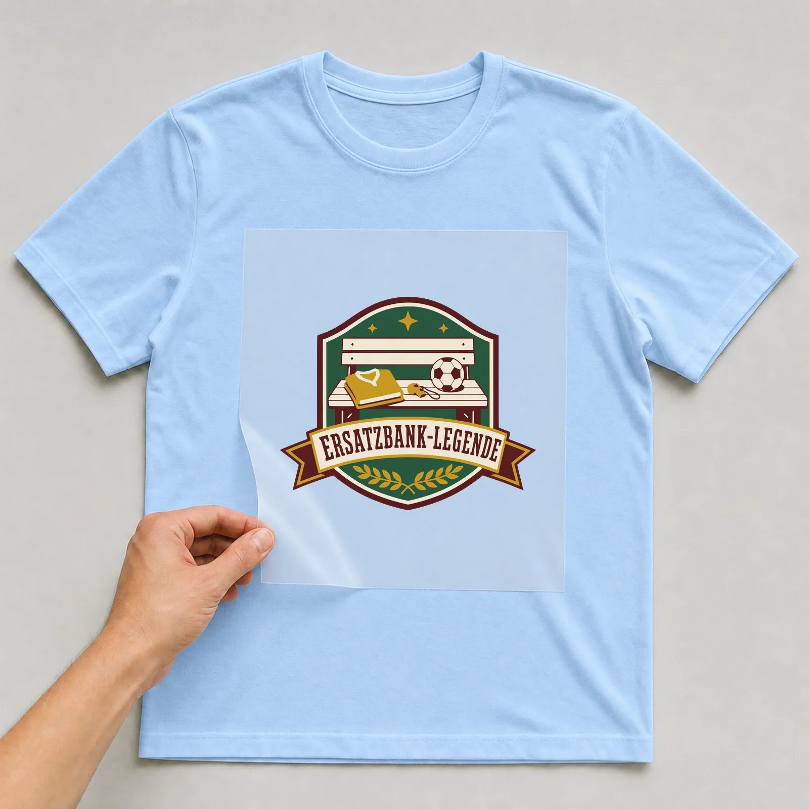 Bügelbild Ersatzbank-Legende auf hellblauem T-Shirt, Folie wird aufgelegt