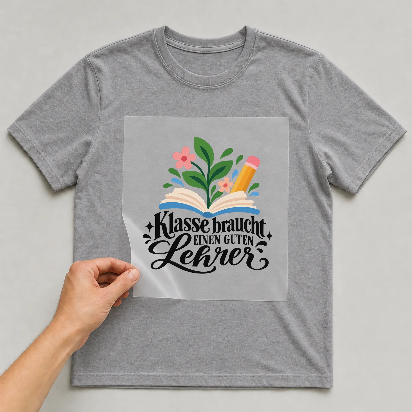 Bügelbild „Klasse braucht einen guten Lehrer“ auf grauem T-Shirt, Folie wird aufgelegt