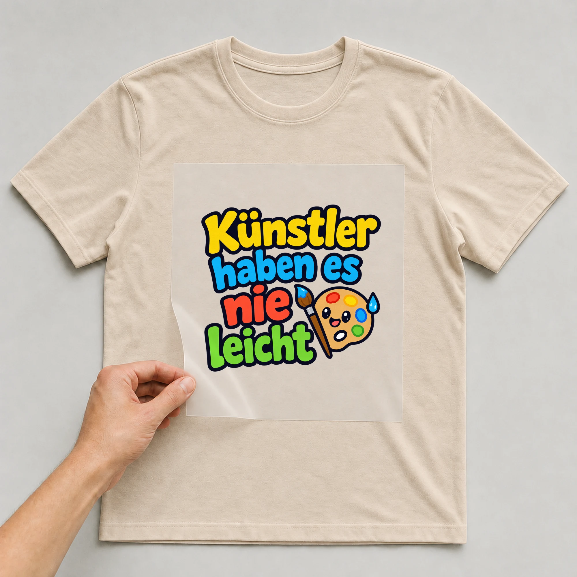 Bügelbild „Künstler haben es nie leicht“ auf beigem T-Shirt, Folie wird aufgelegt