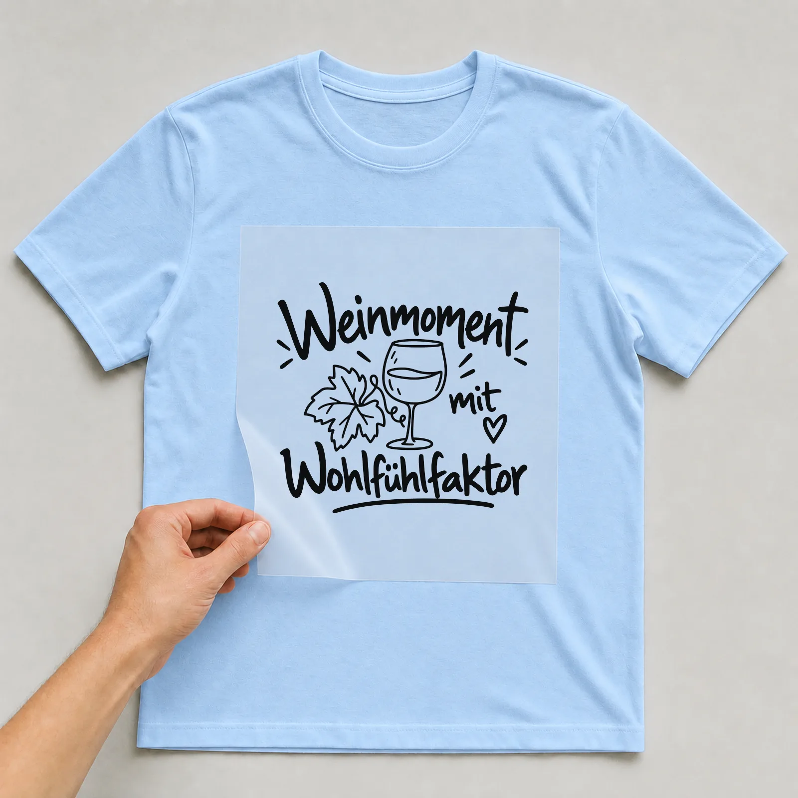 Bügelbild „Weinmoment mit Wohlfühlfaktor“ auf hellblauem T-Shirt, Folie wird aufgelegt