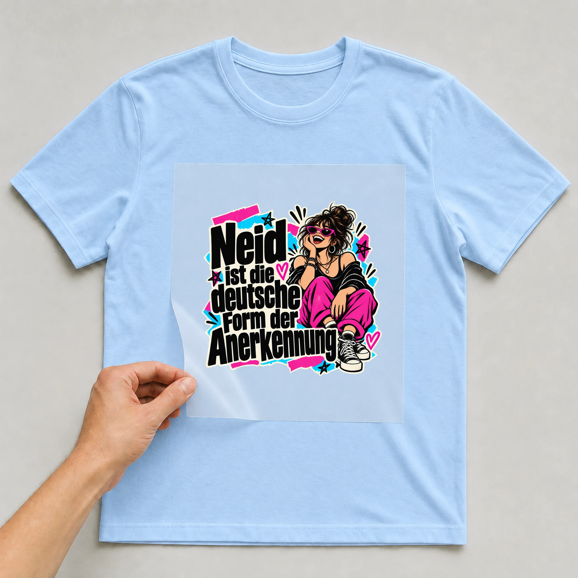 Bügelbild „Neid ist die deutsche Form der Anerkennung“ auf babyblauem T-Shirt, Folie wird aufgelegt