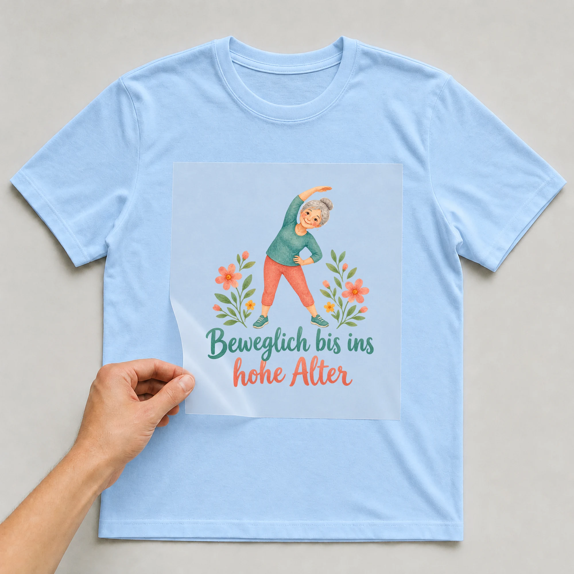 Bügelbild „Beweglich bis ins hohe Alter“ auf babyblauem T-Shirt, Folie wird aufgelegt