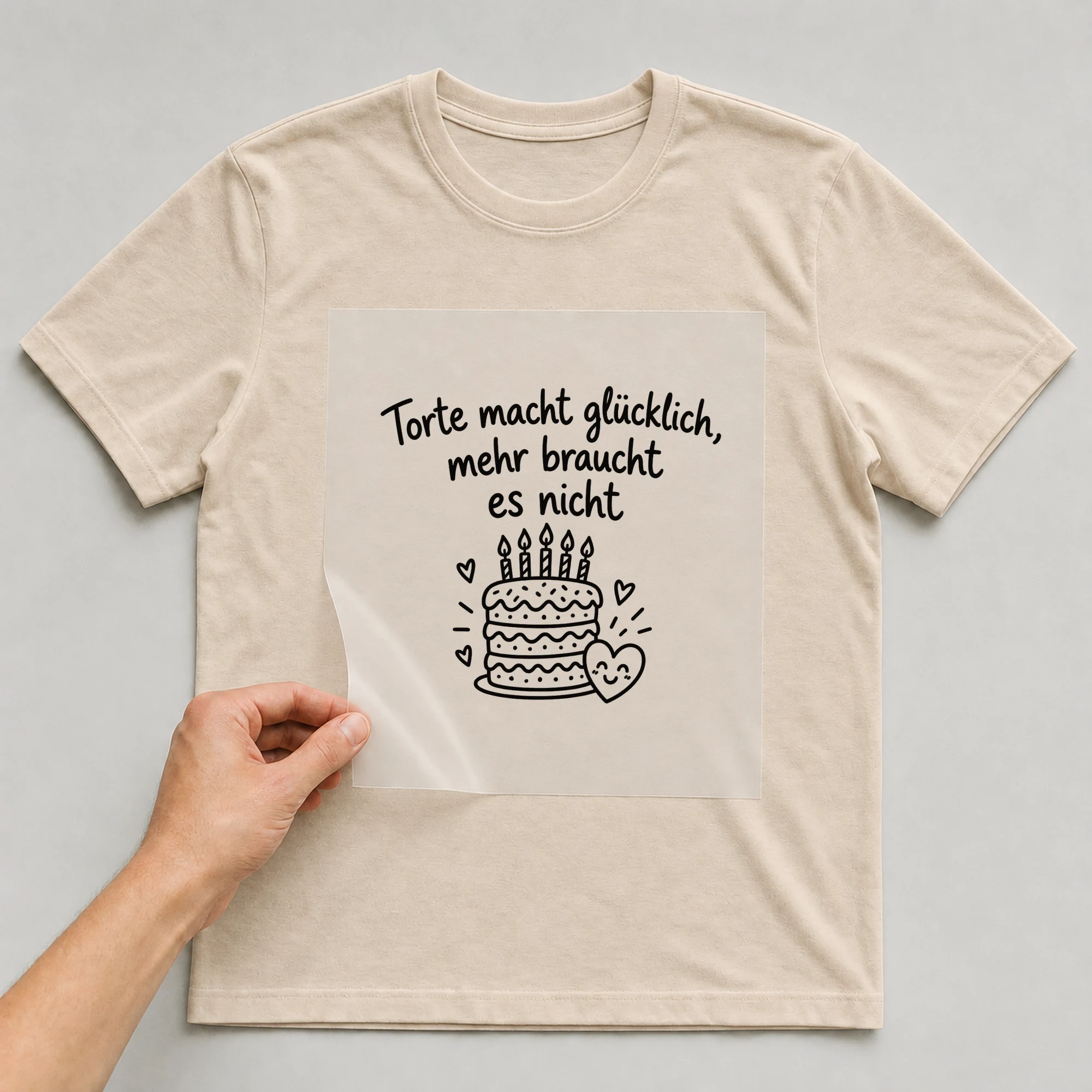 Bügelbild „Torte macht glücklich, mehr braucht es nicht“ auf beigem T-Shirt, Folie wird aufgelegt