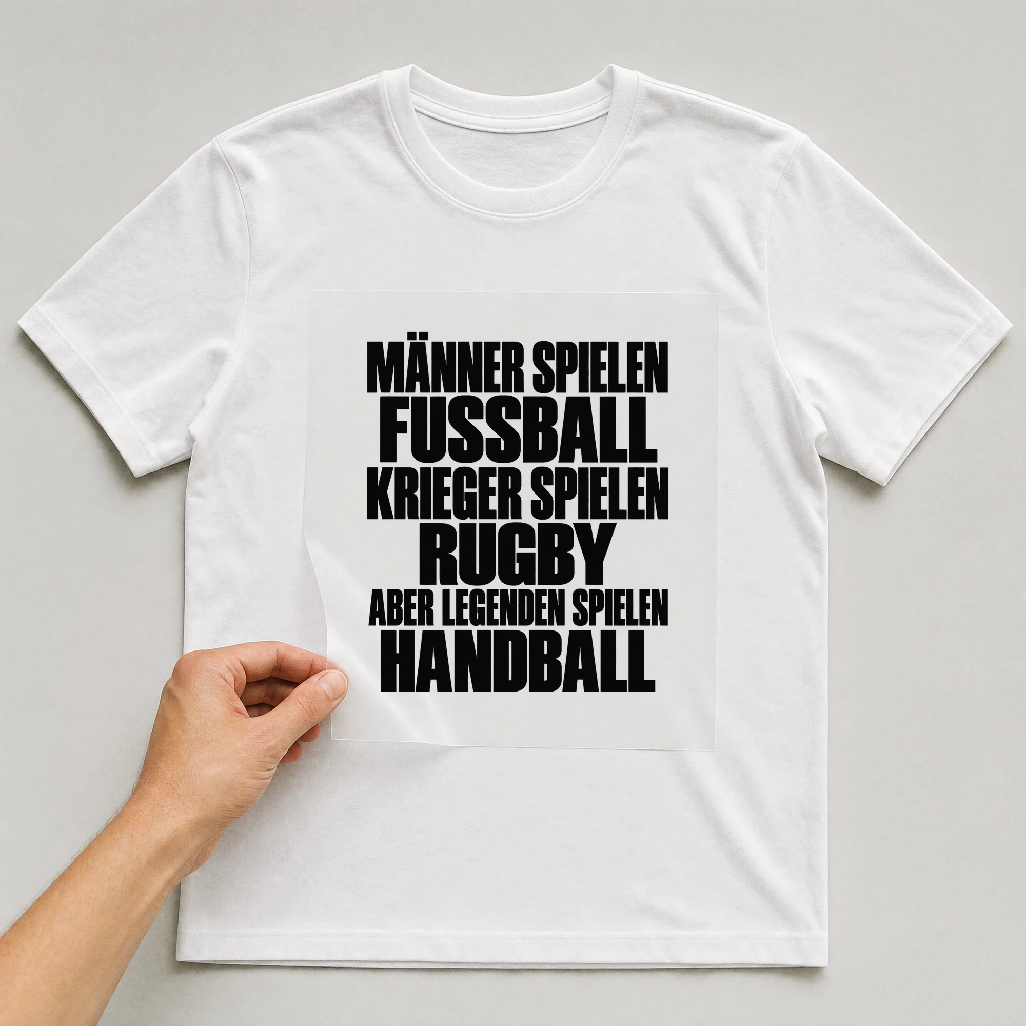 Bügelbild „Männer spielen Fußball Krieger spielen Rugby aber Legenden spielen Handball“ auf weißem T-Shirt, Folie wird aufgelegt