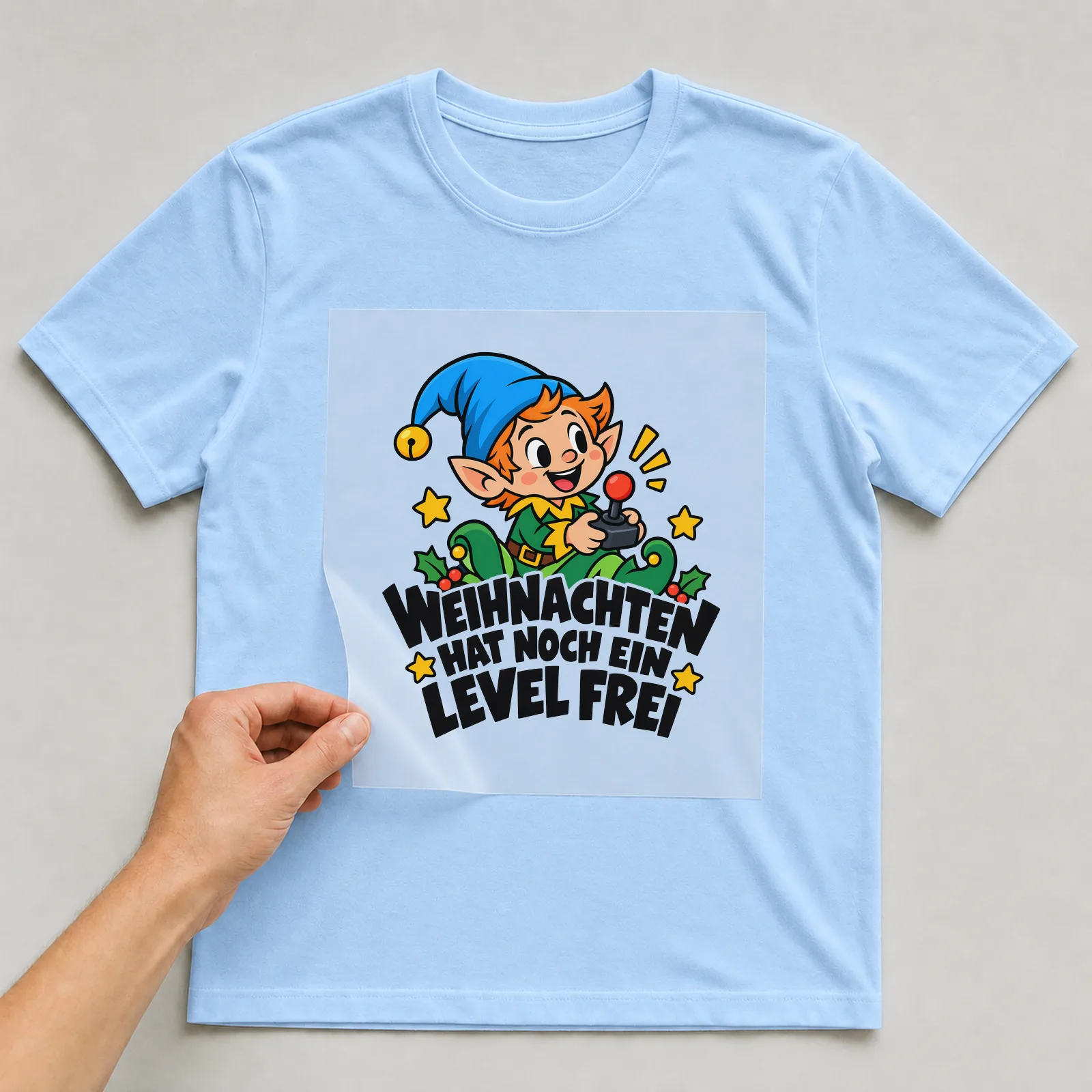Bügelbild „Weihnachten hat noch ein Level frei“ auf hellblauem T-Shirt, Folie wird aufgelegt