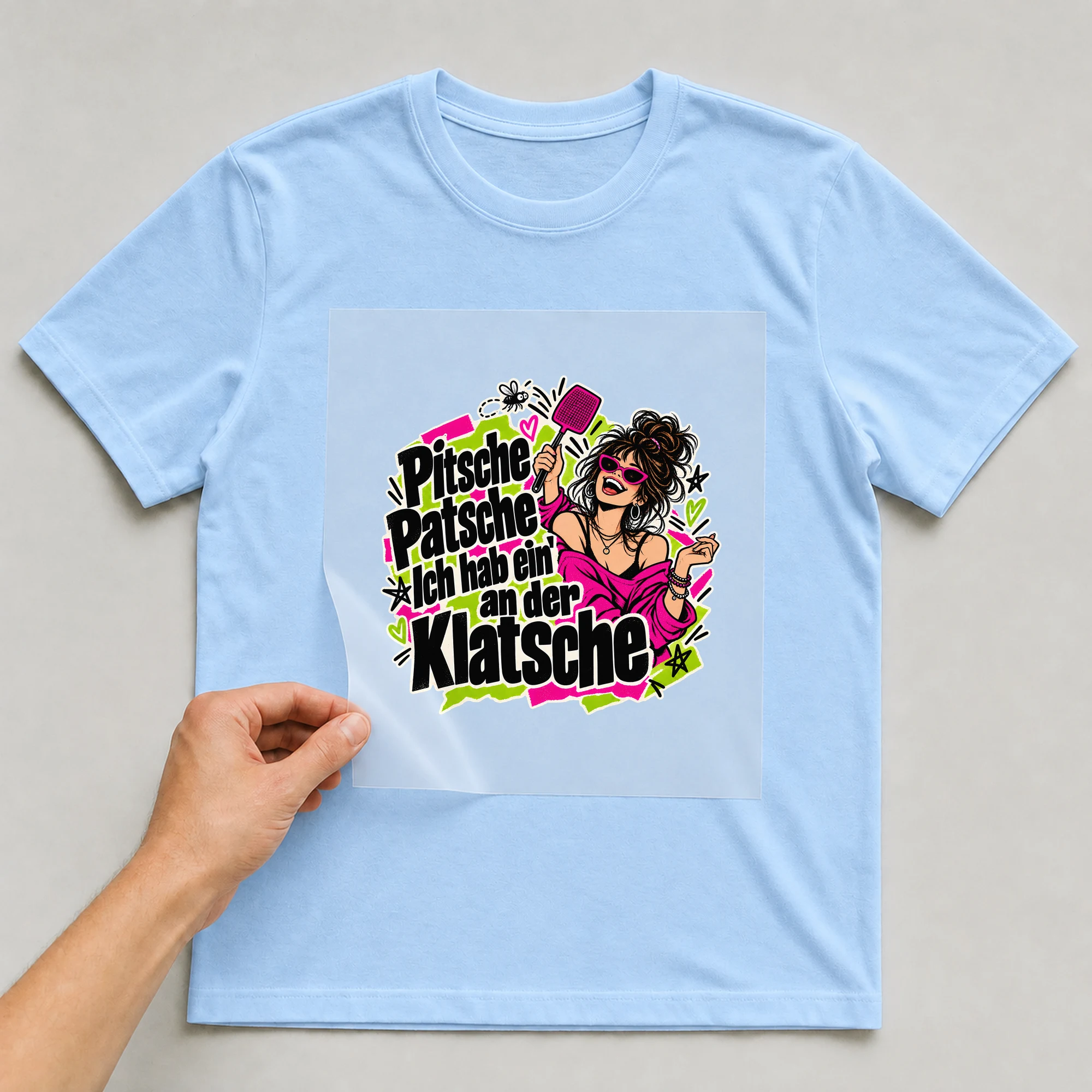 Bügelbild „Pitsche Patsche Ich hab ein' an der Klatsche“ auf babyblauem T-Shirt, Folie wird aufgelegt