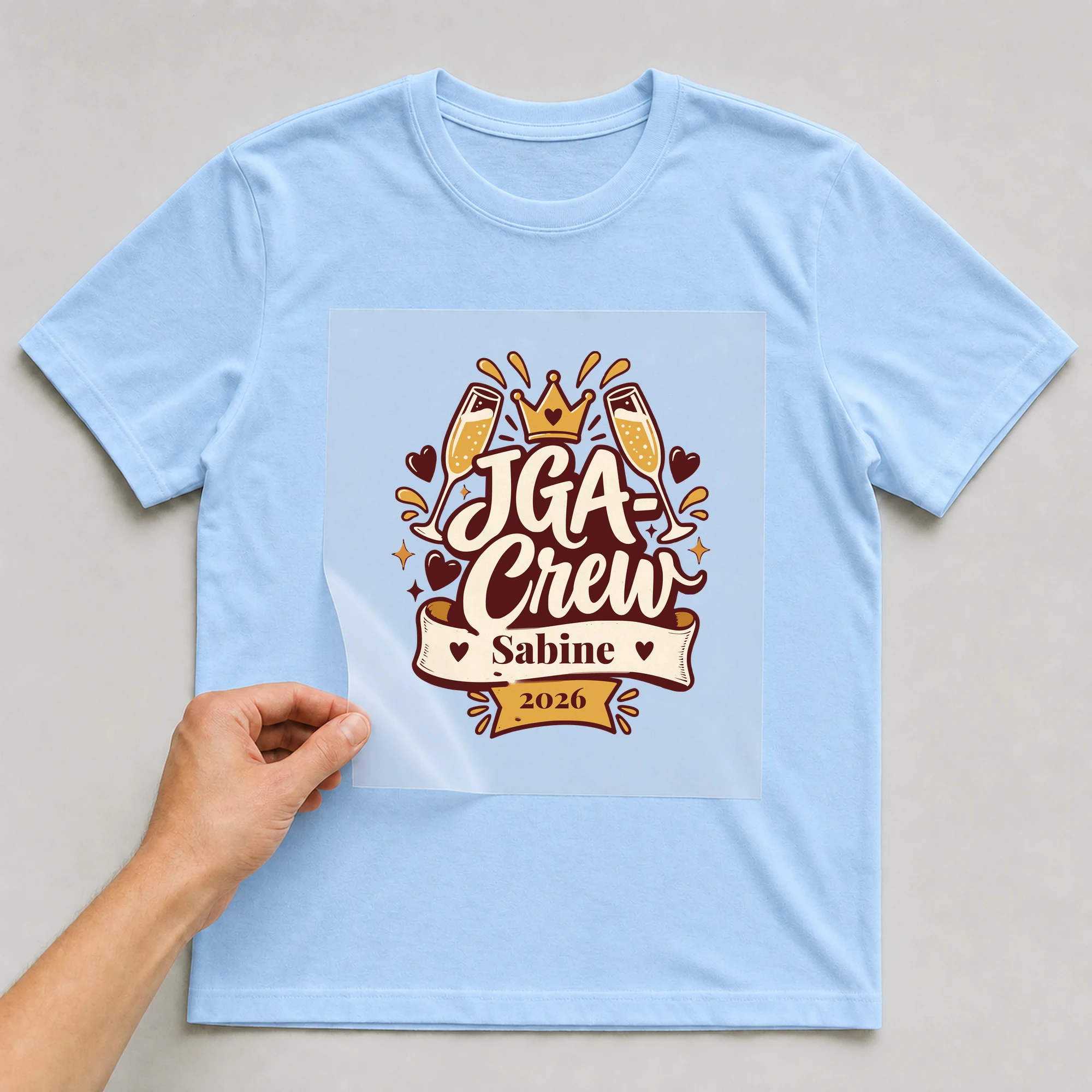Bügelbild JGA-Crew mit Name und Jahr auf hellblauem T-Shirt, Folie wird aufgelegt