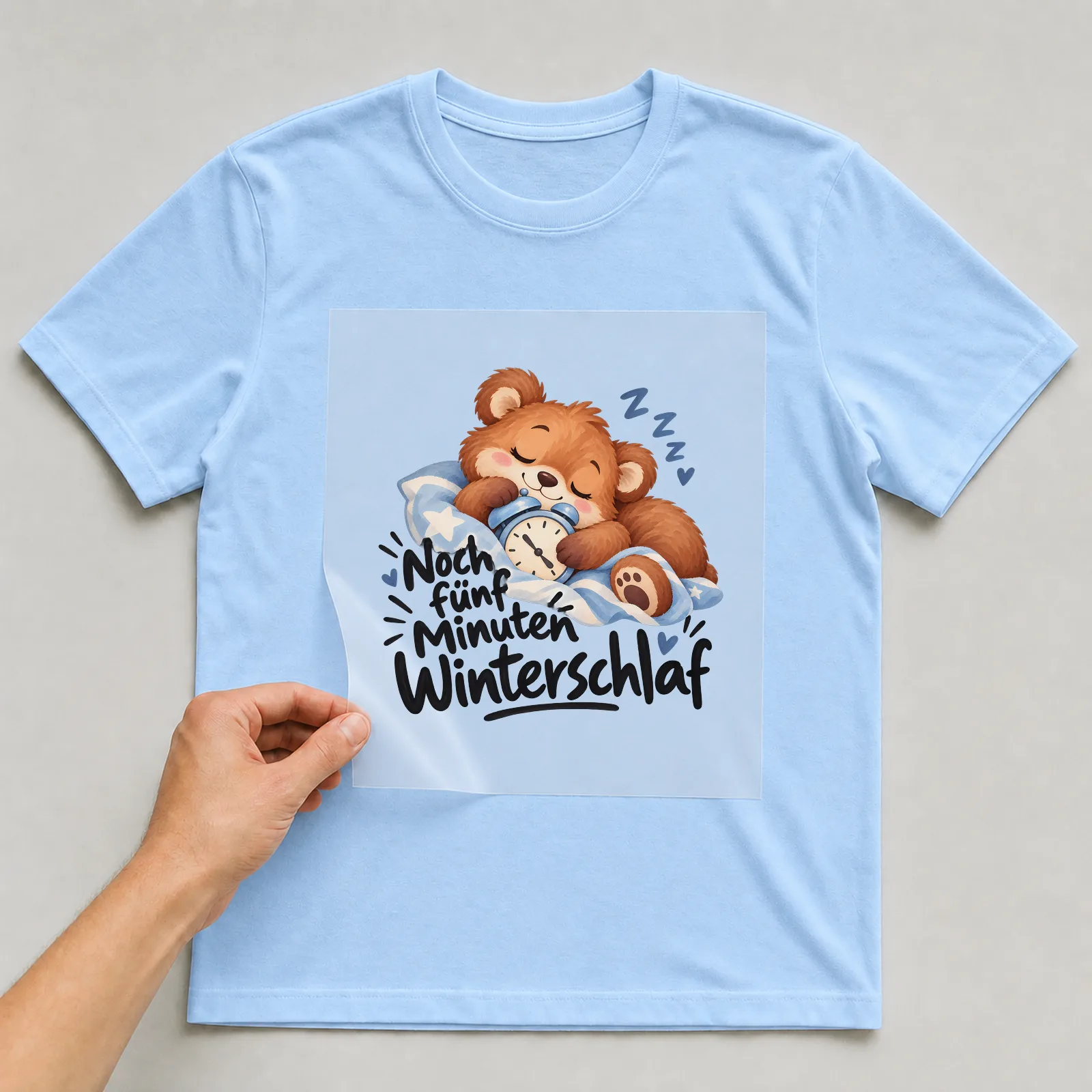 Bügelbild „Noch fünf Minuten Winterschlaf“ auf hellblauem T-Shirt, Folie wird aufgelegt