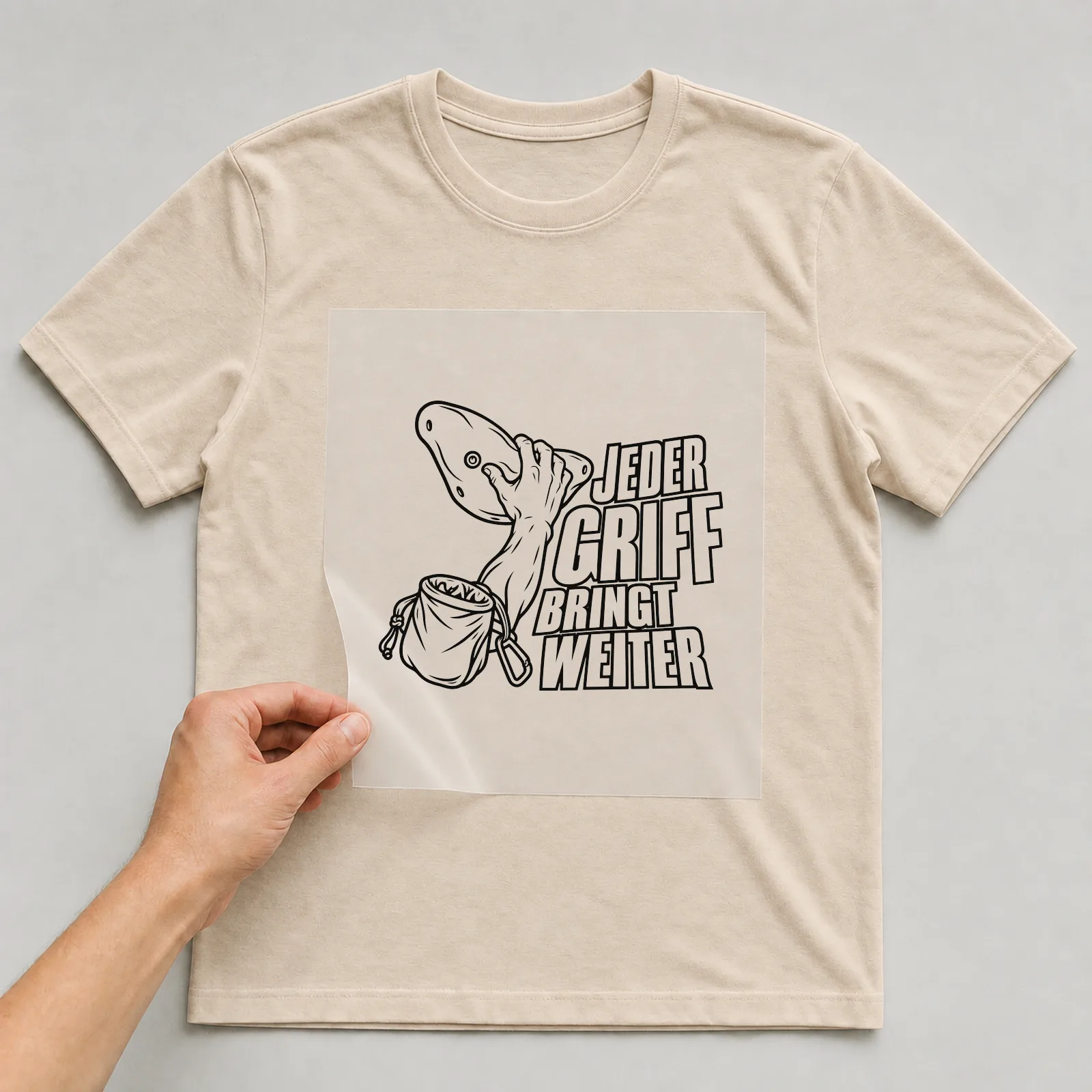 Bügelbild „Jeder Griff bringt weiter“ auf beigem T-Shirt, Folie wird aufgelegt