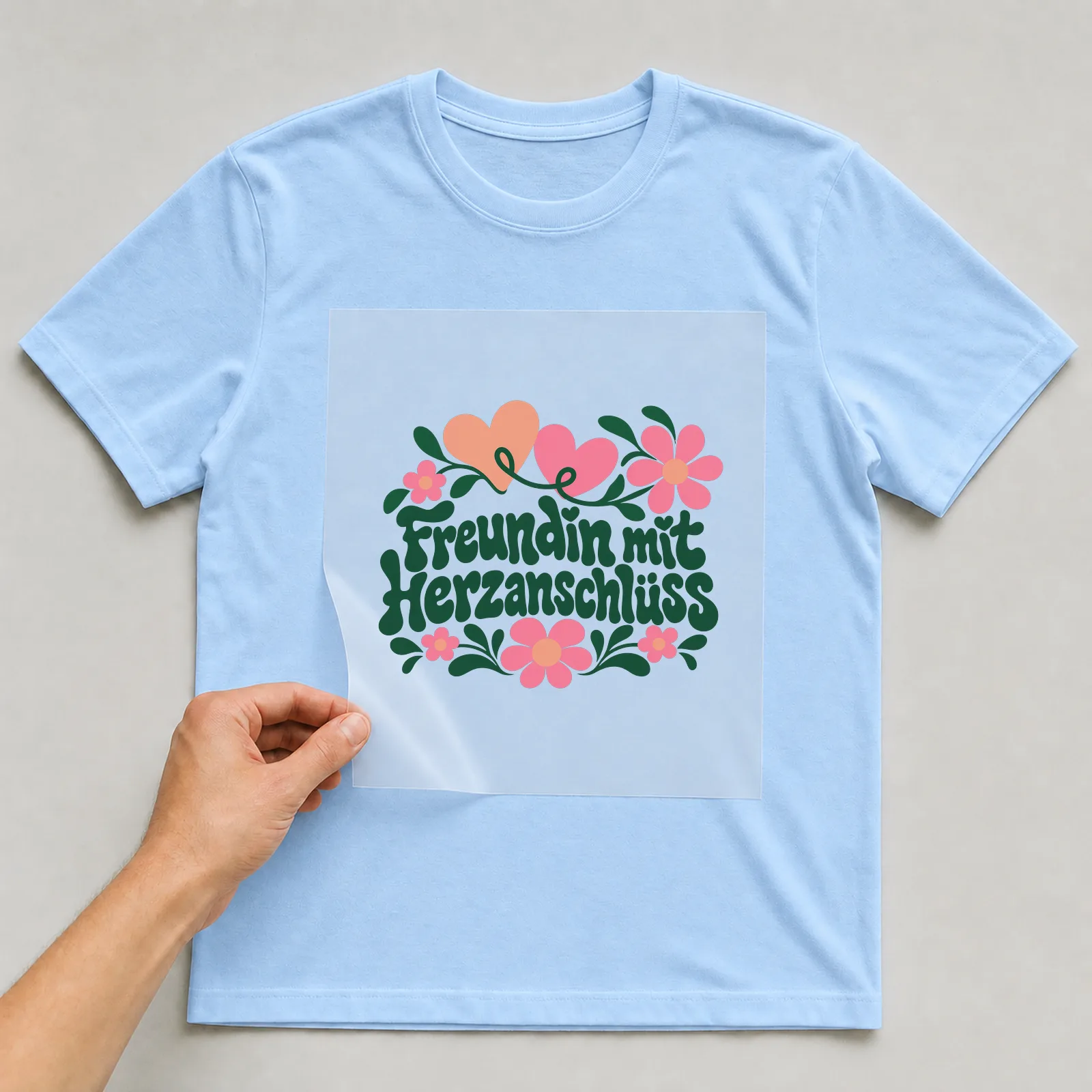 Bügelbild „Freundin mit Herzanschluss“ auf hellblauem T-Shirt, Folie wird aufgelegt