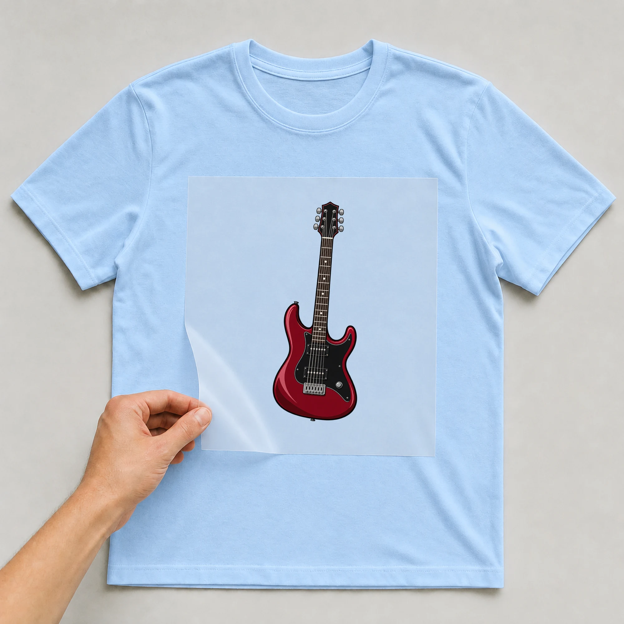 Bügelbild „Rock And Roll Gitarre“ auf babyblauem T-Shirt, Folie wird aufgelegt