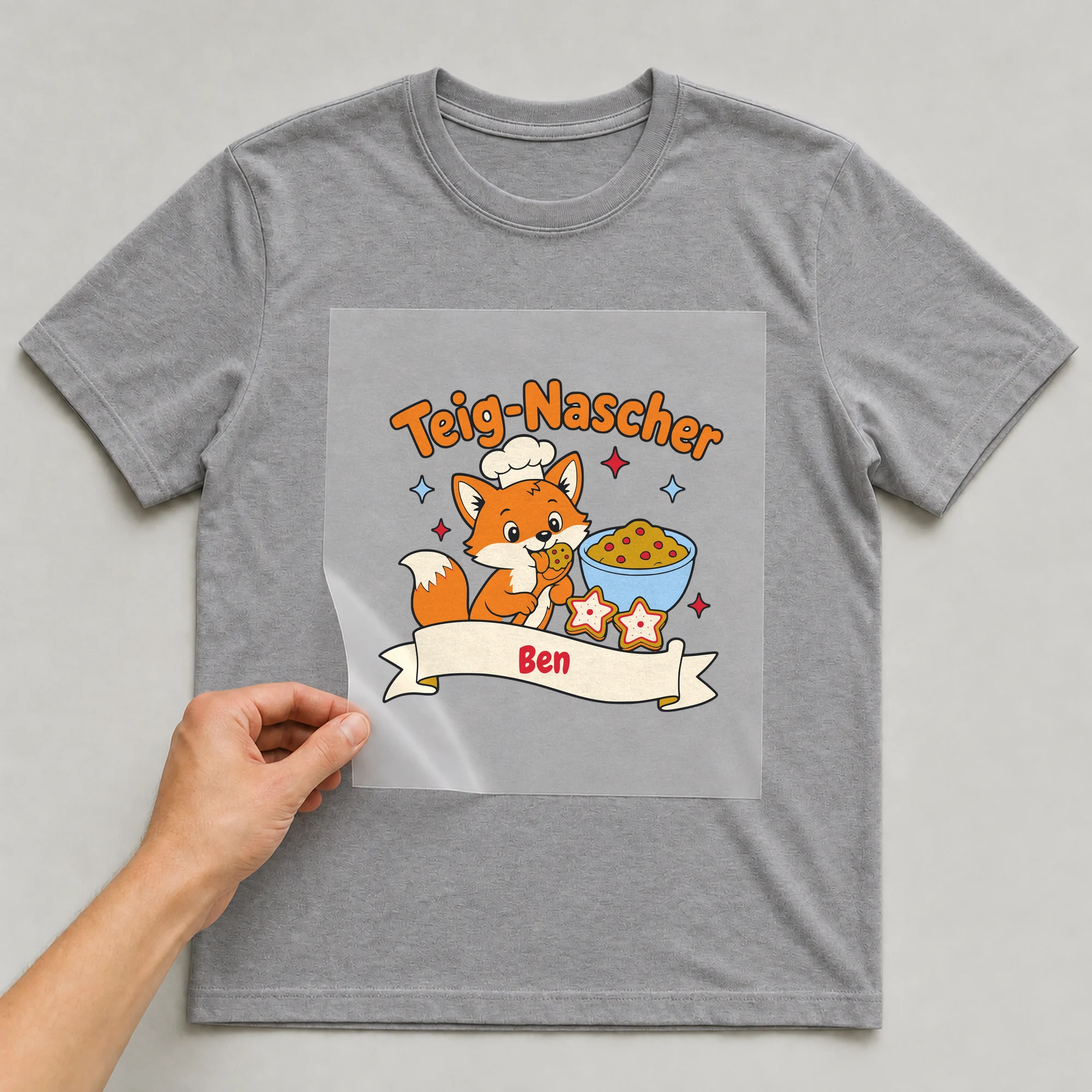 Bügelbild Teig-Nascher mit Name auf grauem T-Shirt, Folie wird aufgelegt