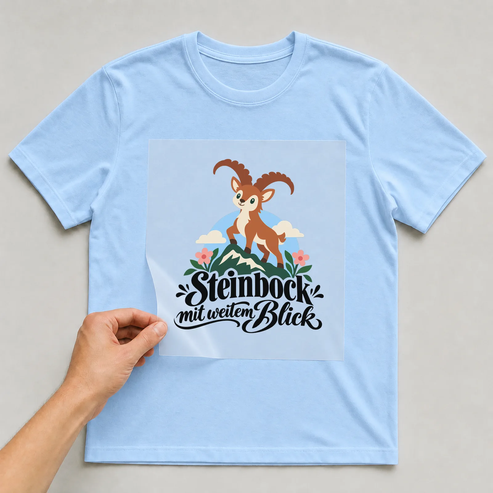 Bügelbild „Steinbock mit weitem Blick“ auf hellblauem T-Shirt, Folie wird aufgelegt