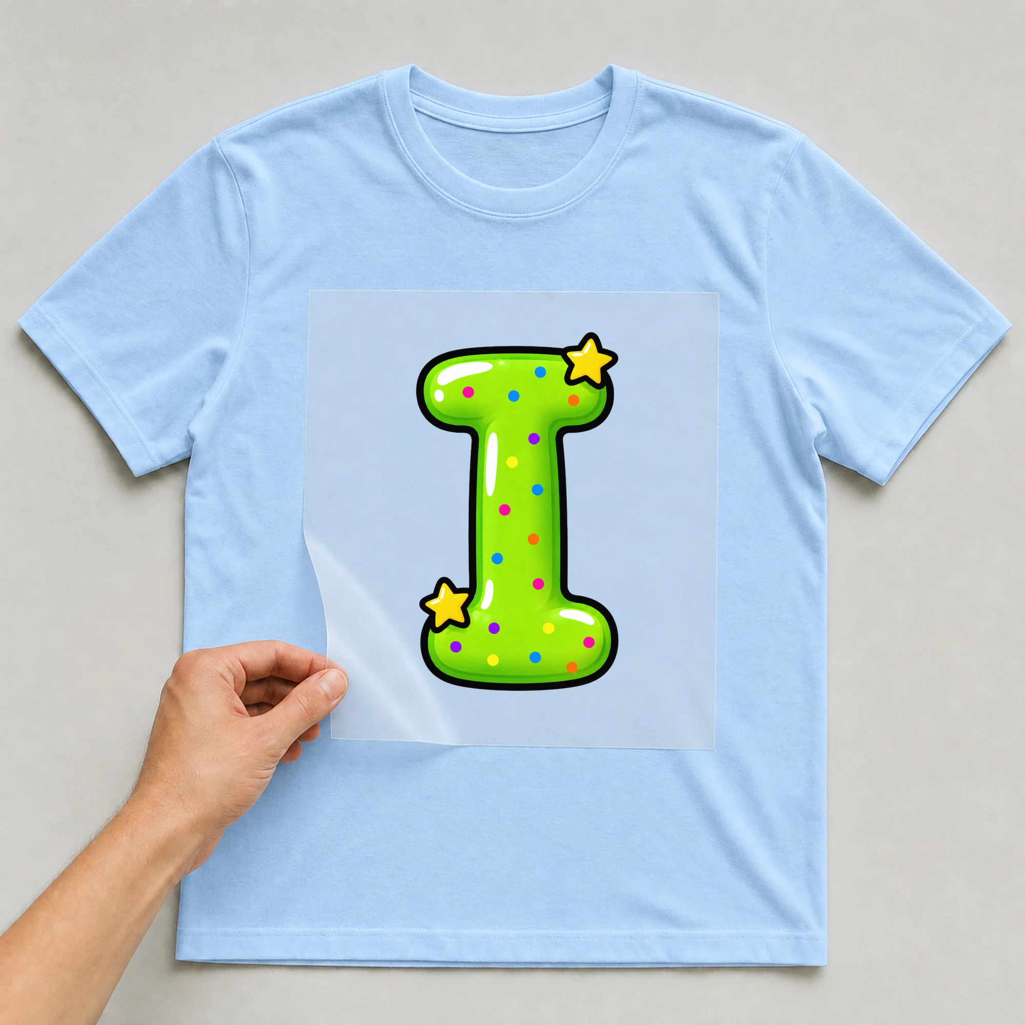 Bügelbild „Buchstabe I im Comic-Ballon-Stil“ auf babyblauem T-Shirt, Folie wird aufgelegt