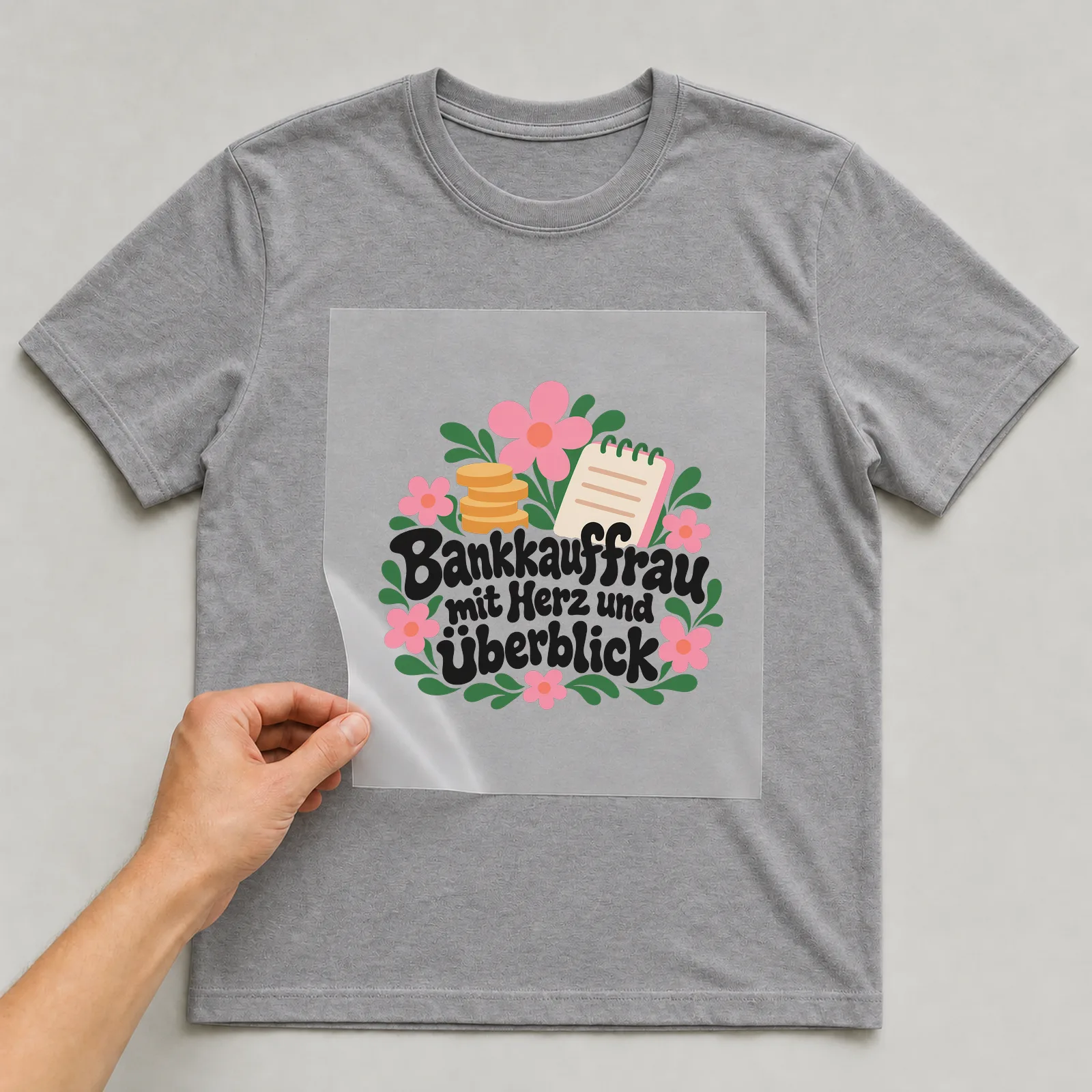 Bügelbild „Bankkauffrau mit Herz und Überblick“ auf grauem T-Shirt, Folie wird aufgelegt