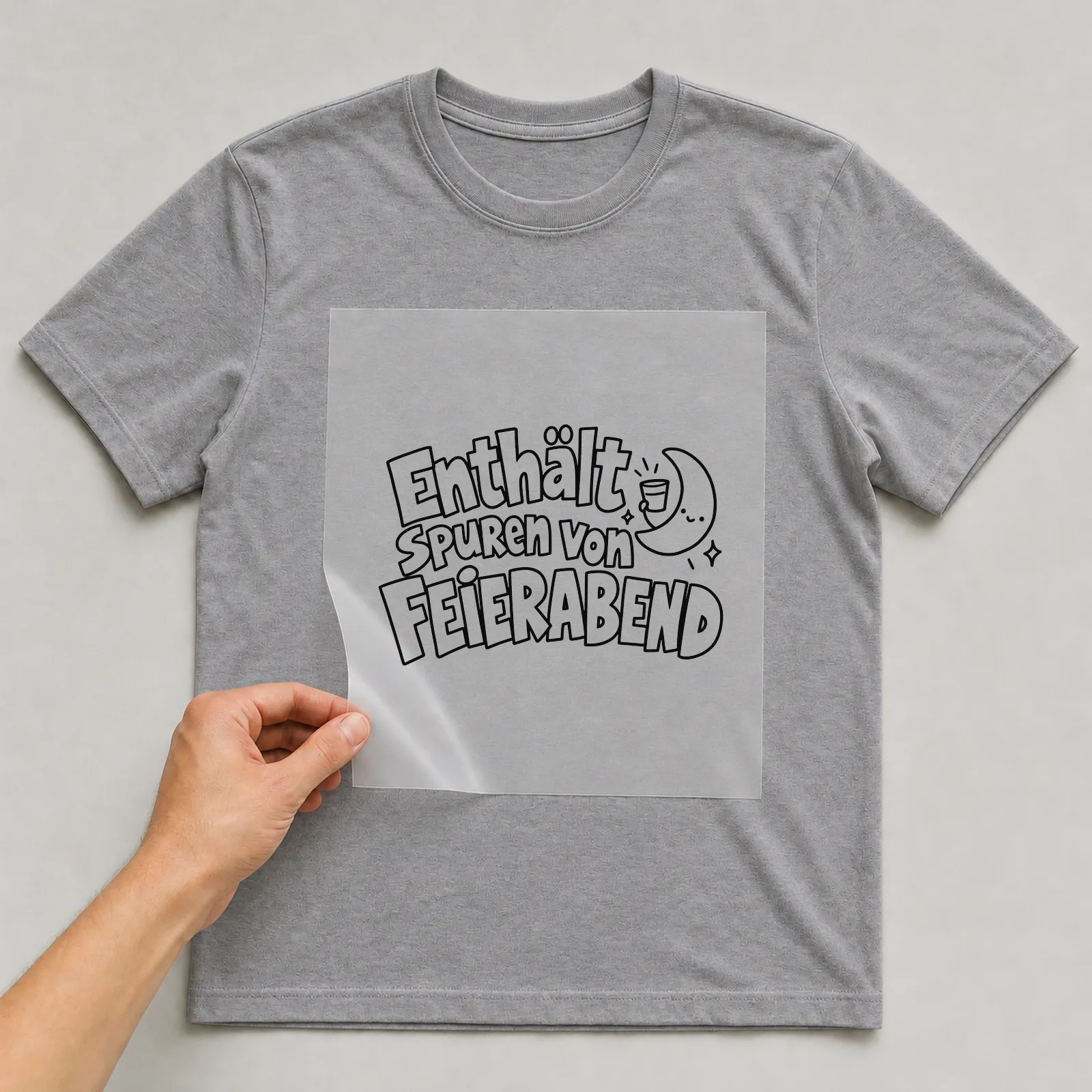 Bügelbild „Enthält Spuren von Feierabend“ auf grauem T-Shirt, Folie wird aufgelegt